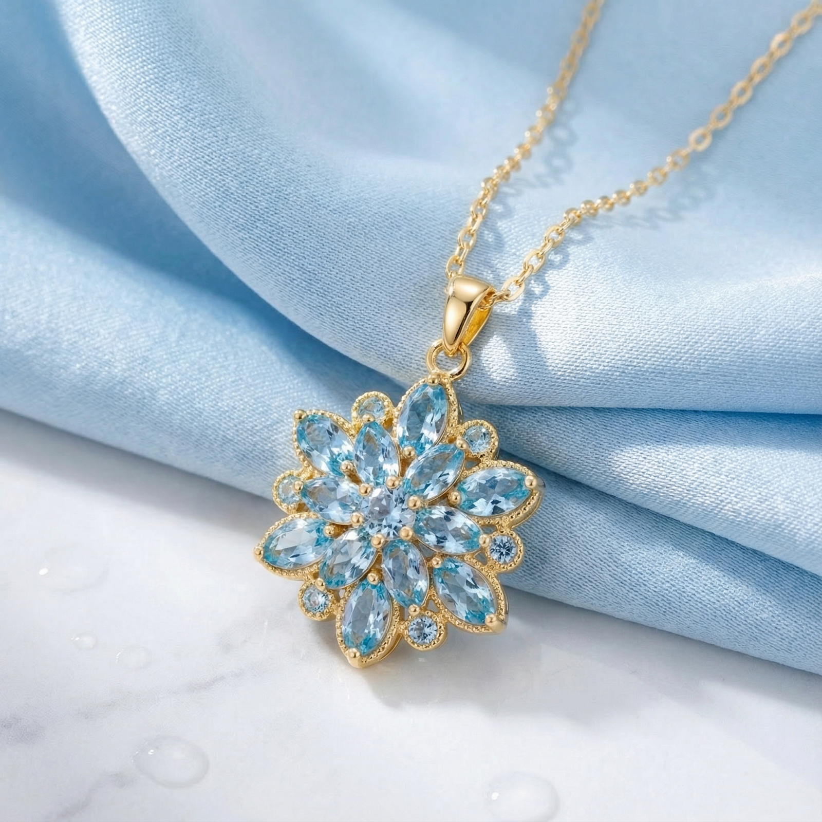 Gold stainless steel necklace with a marquise-cut simulated aquamarine flower pendant on blue fabric and marble.