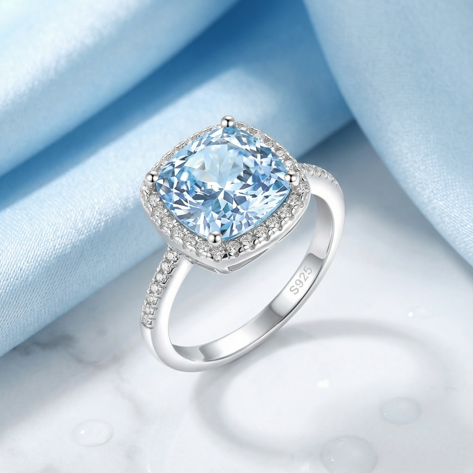 Cushion-cut simulated aquamarine halo ring in S925 sterling silver on blue silk and marble.