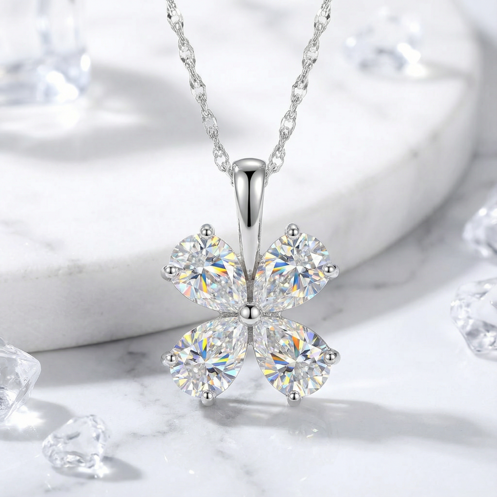 Sterling silver clover necklace with pear-cut zirconia stones on a white marble surface with crystal accents.