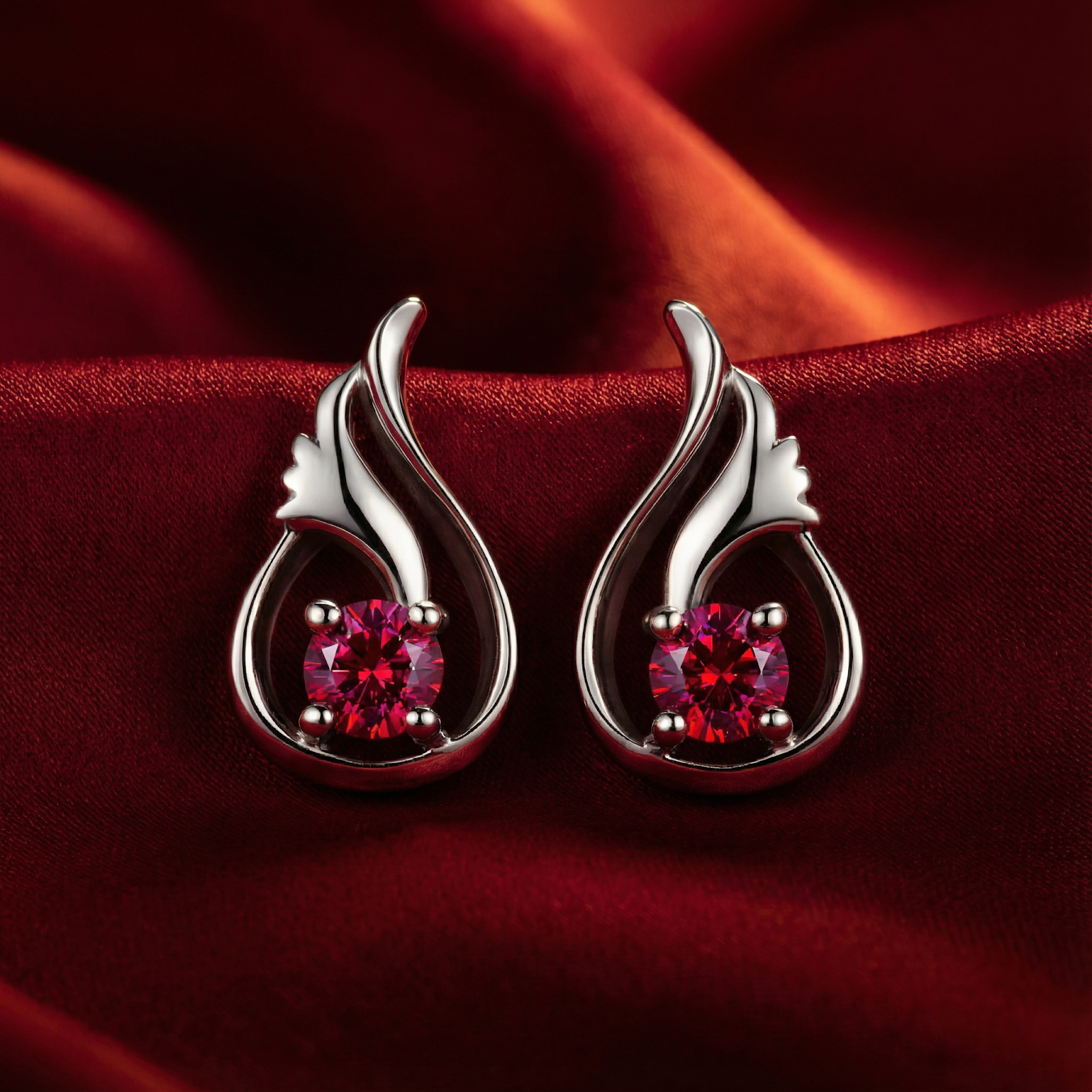 Round cut simulated ruby earrings in platinum vermeil sterling silver on a red silk background.