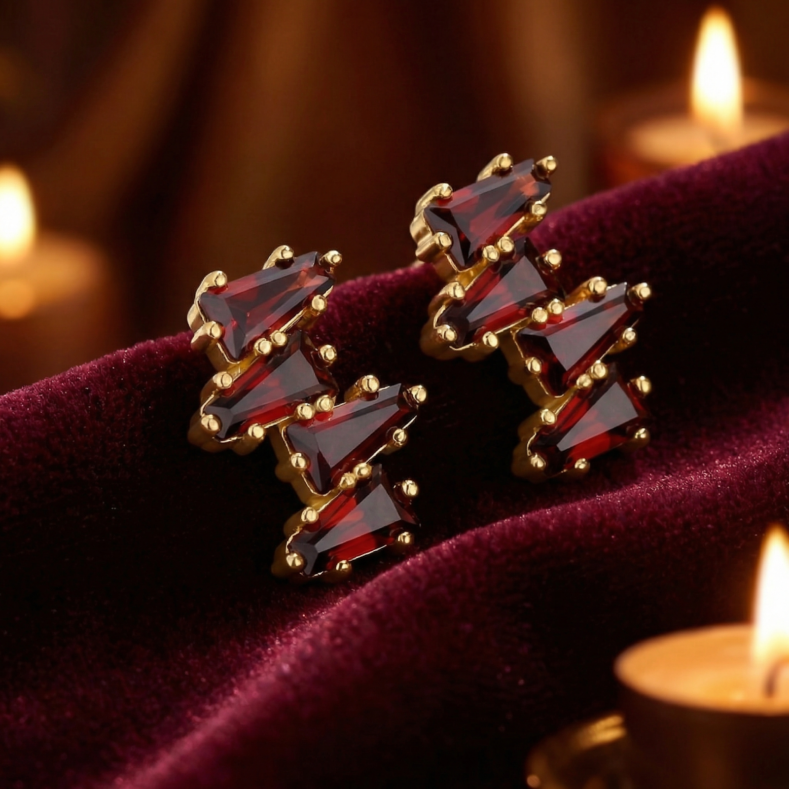 Red simulated garnet cluster earrings in 18K gold vermeil on dark red velvet with warm candle lighting.