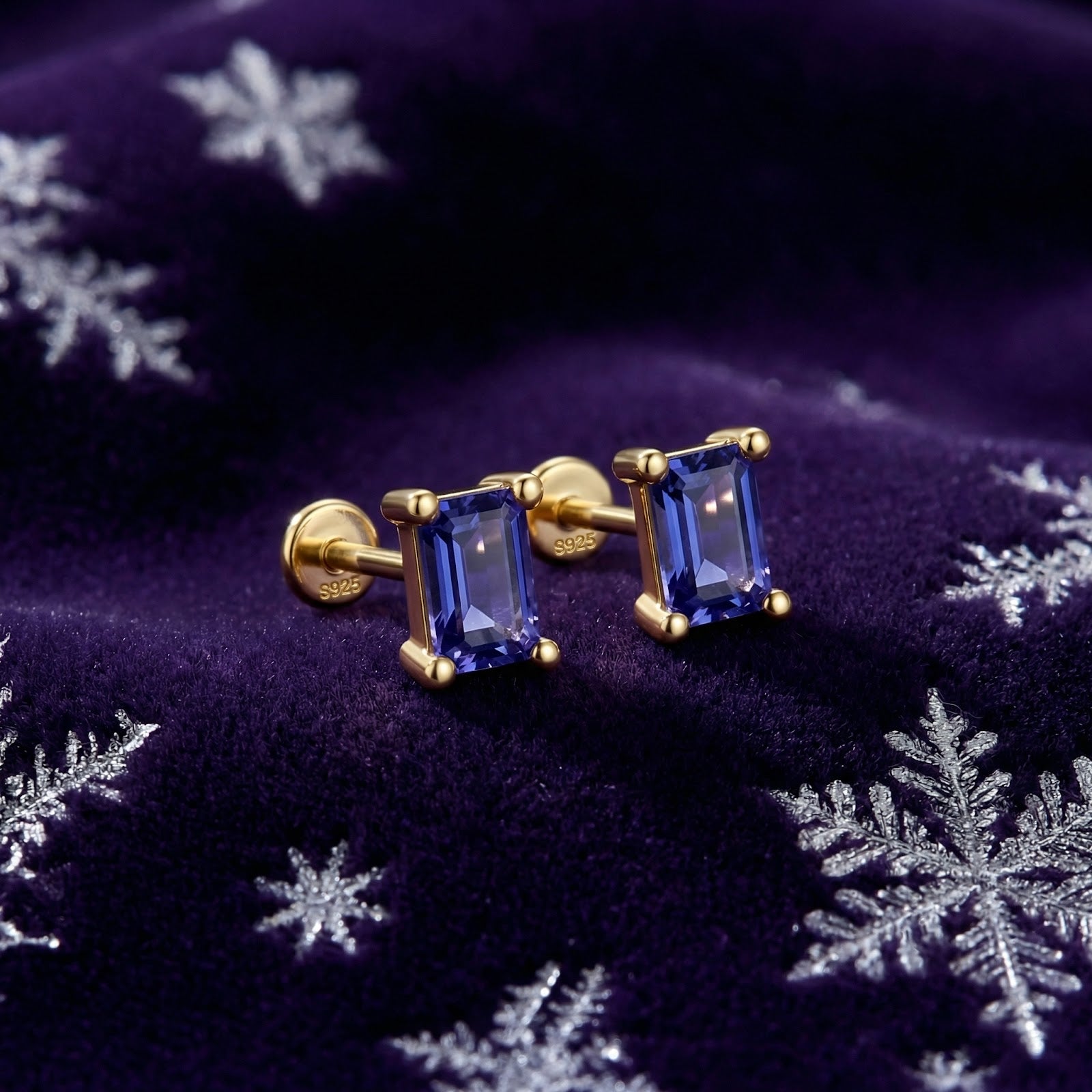 Emerald-cut simulated tanzanite stud earrings in 18K gold vermeil on a festive purple snowflake background.