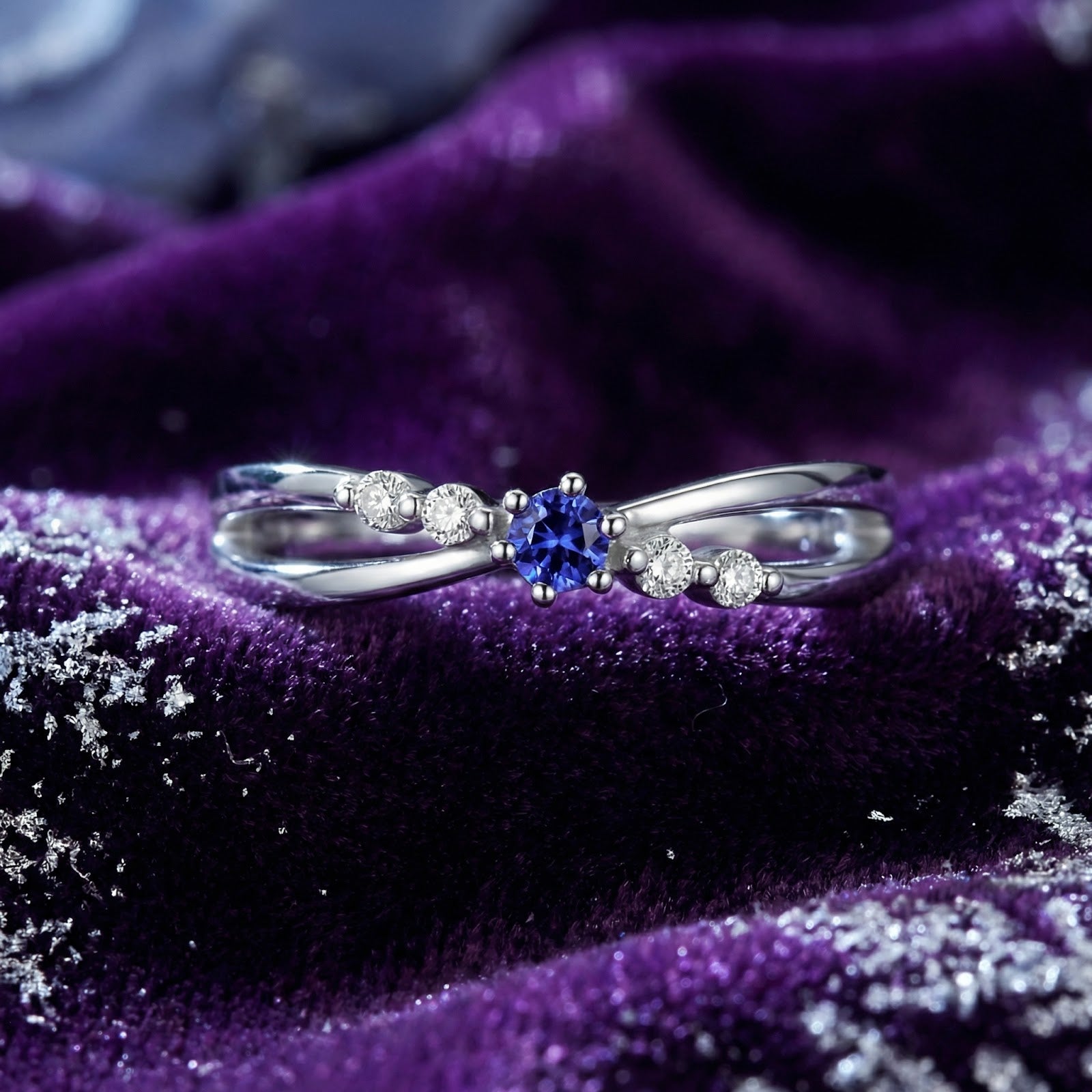 S925 sterling silver crossover ring with round-cut simulated tanzanite on a purple velvet background.