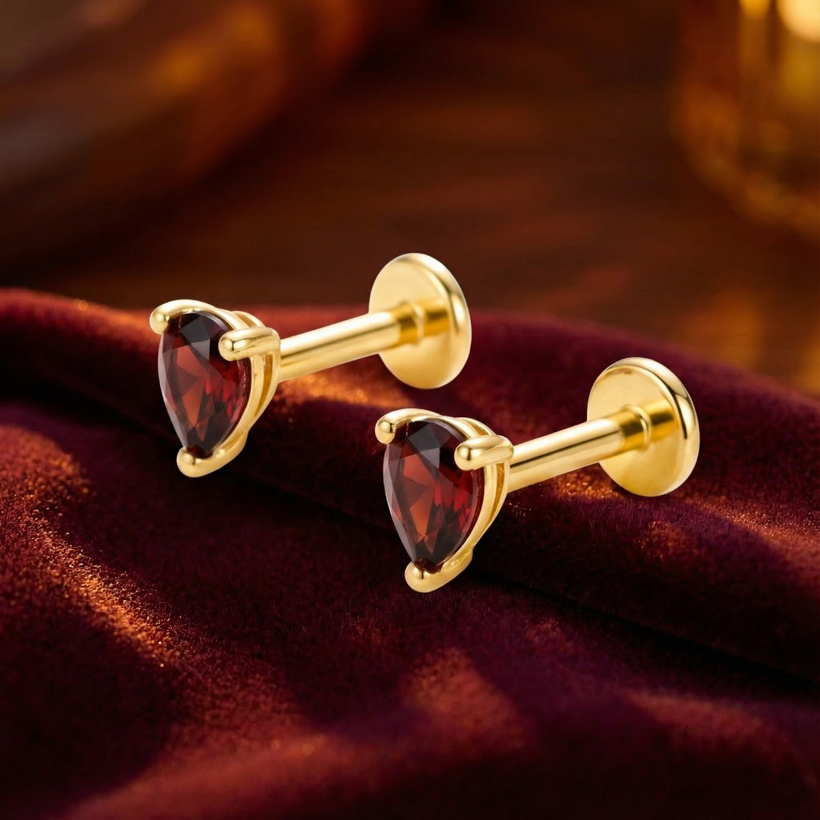 Pear cut simulated garnet stud earrings in 18K gold vermeil resting on dark red velvet.