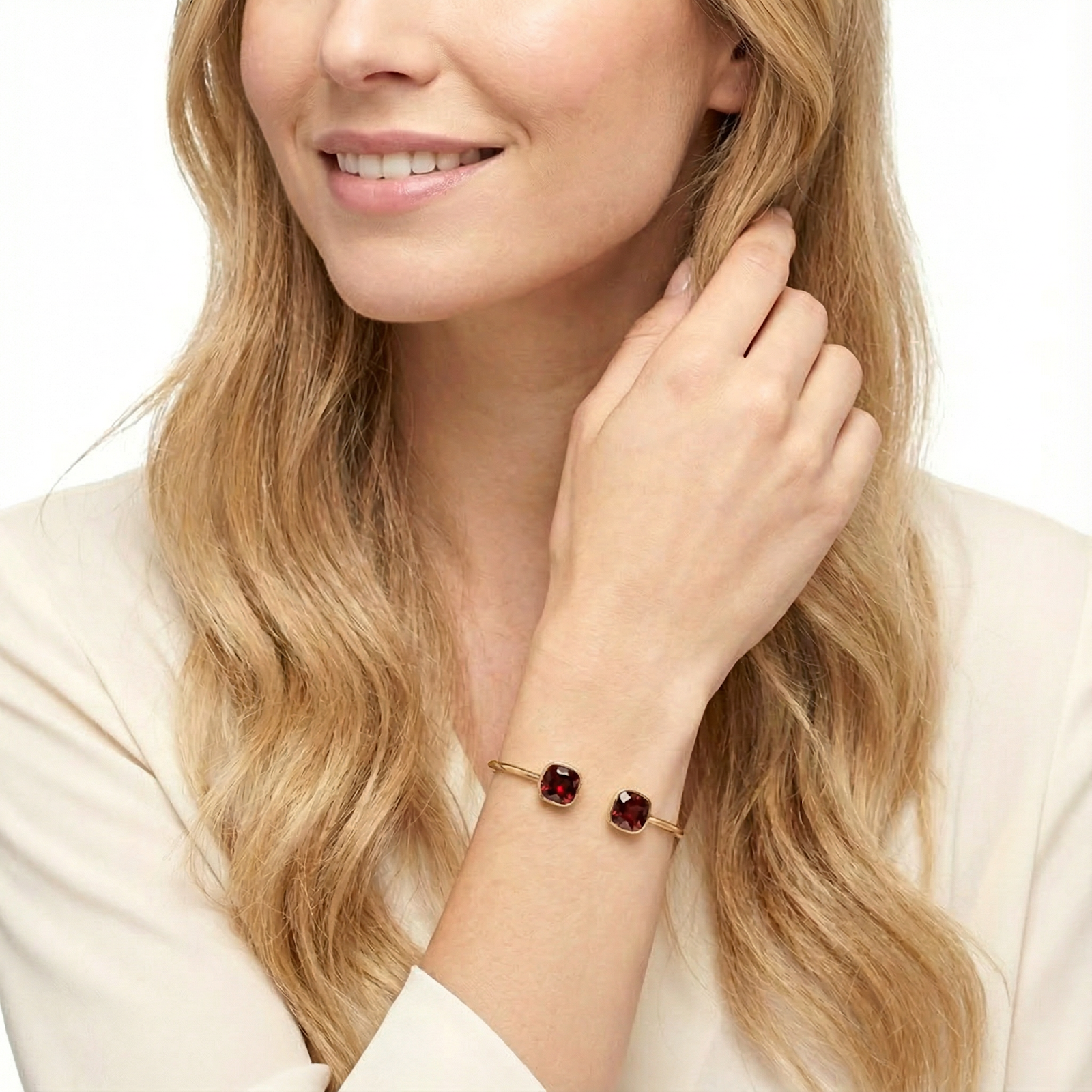 Gold cuff bracelet with halo-set red square cushion-cut simulated garnets worn on a woman's wrist.