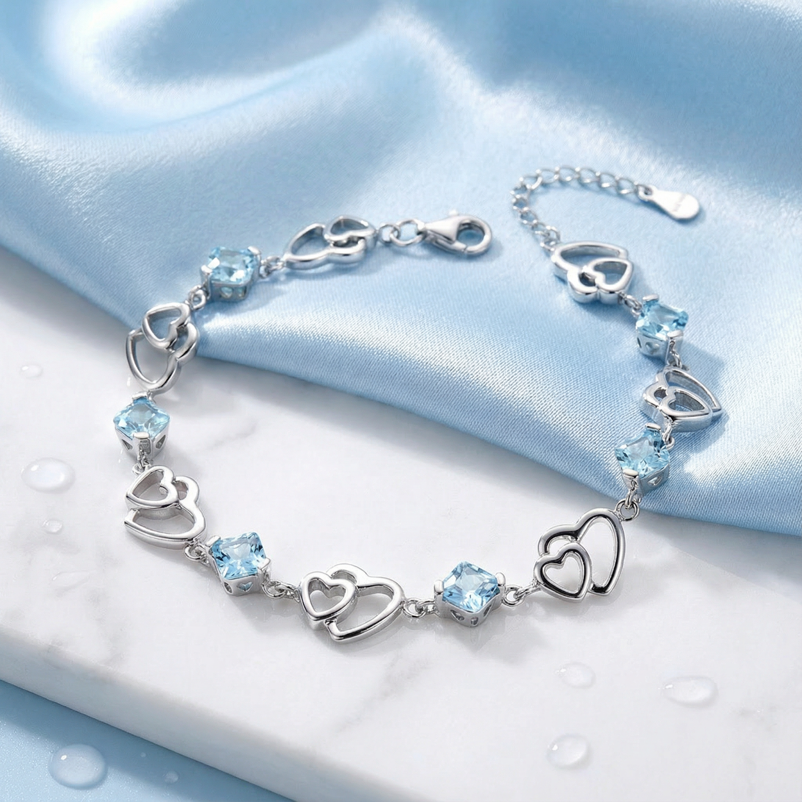 Sterling silver heart link bracelet with square cut light blue aquamarine stones on blue silk and marble.