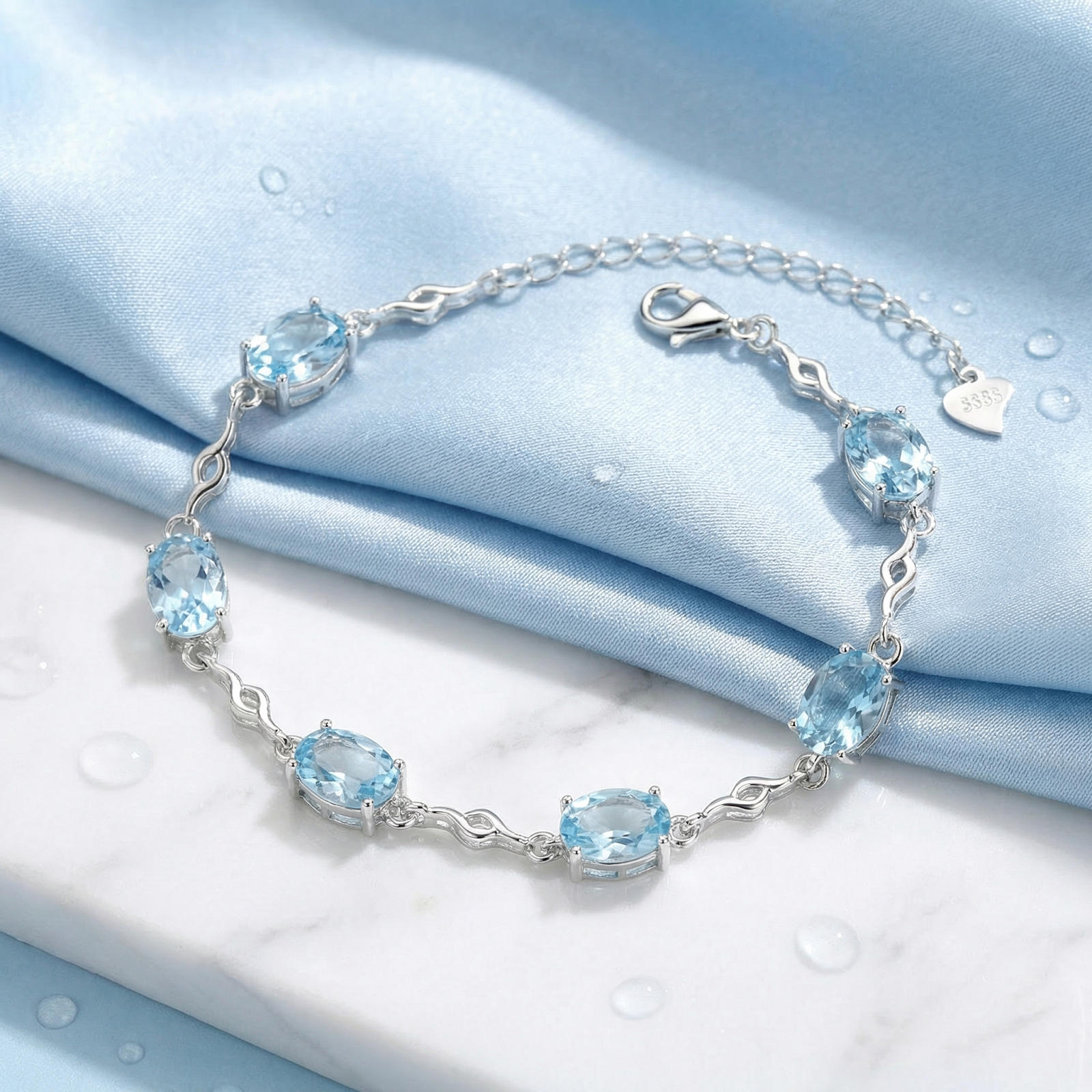 Oval cut simulated aquamarine station bracelet in sterling silver on a blue silk and marble background.
