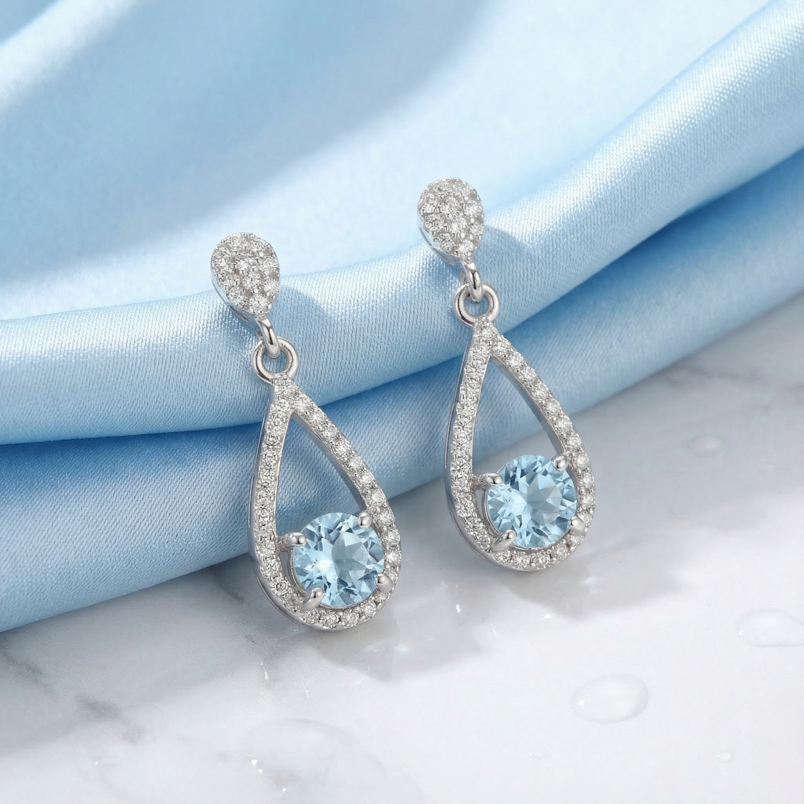 Sterling silver teardrop drop earrings with round simulated aquamarine stones on blue silk and marble.