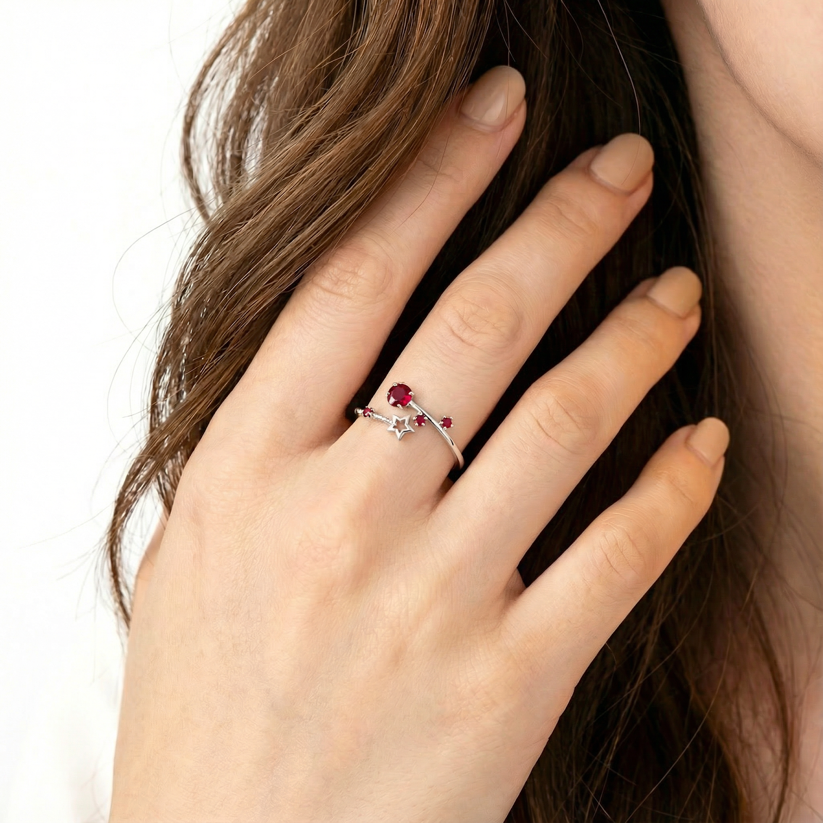 Woman wearing the Lyriana star bypass ring in sterling silver with red simulated ruby accents.