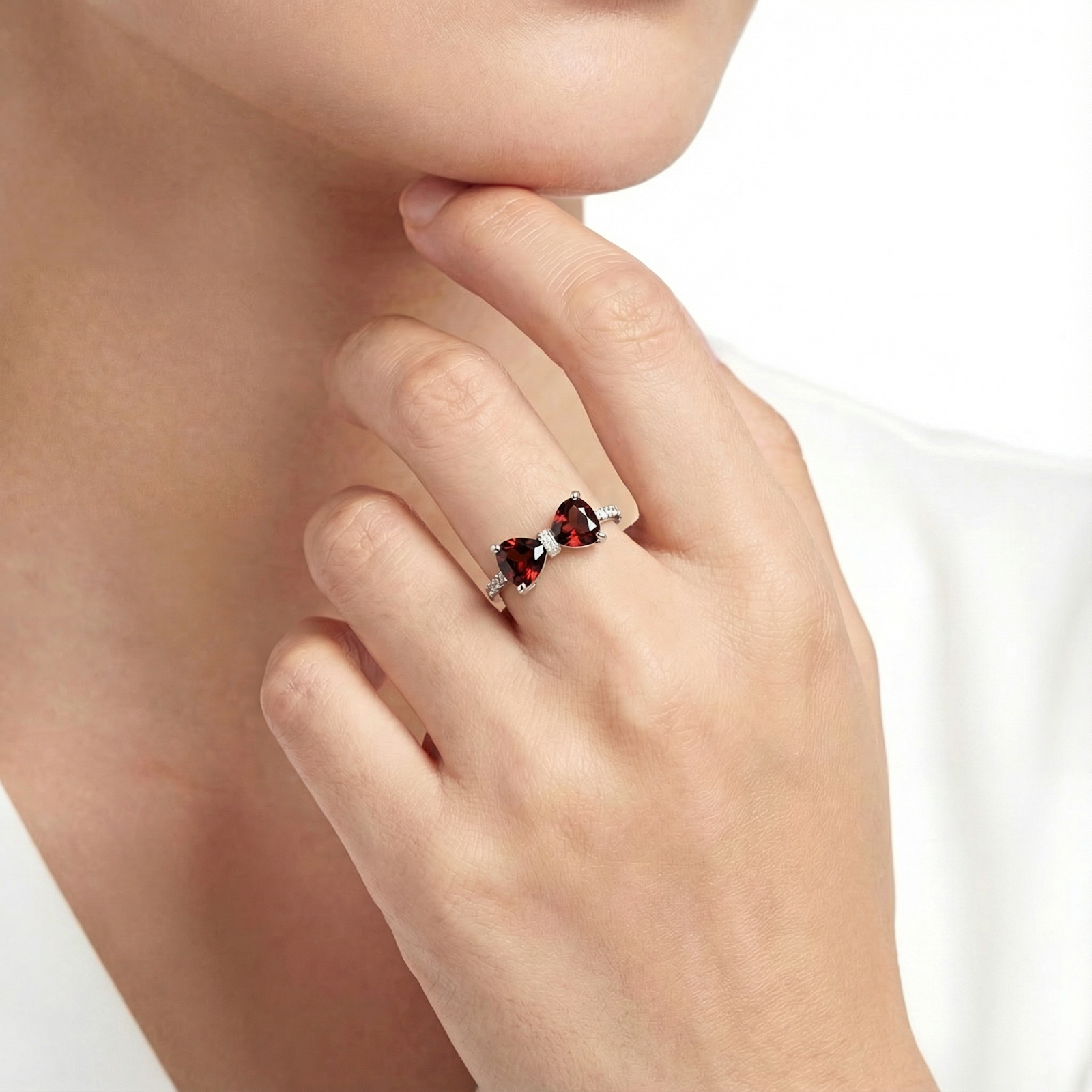 Sterling silver bow ring with red trillion cut simulated garnets worn on a woman's hand.