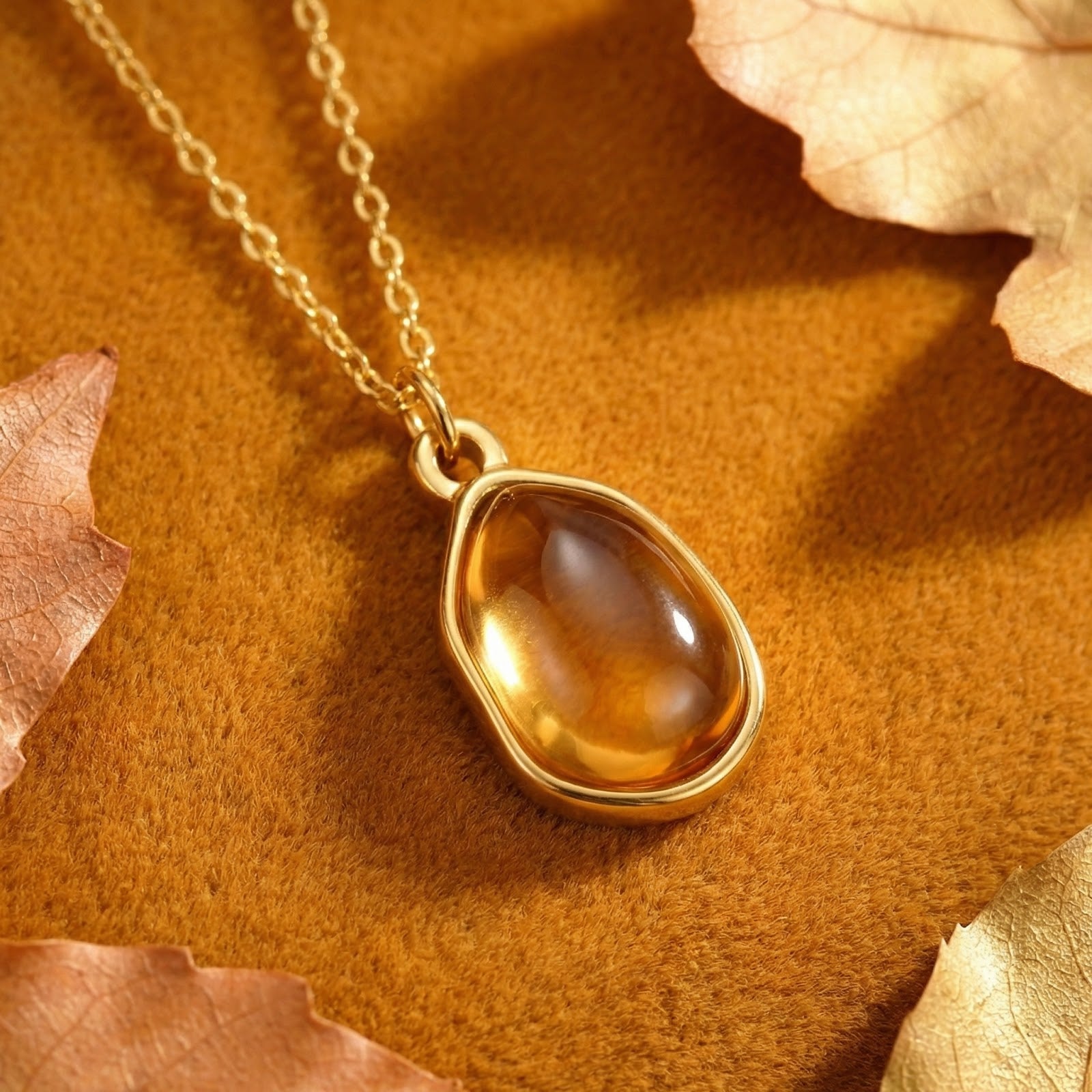 Gold finish stainless steel teardrop necklace with honeyed simulated topaz on a warm surface with autumn leaves.