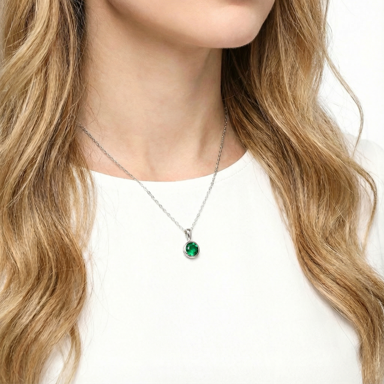 Woman wearing the Elisenne silver bezel necklace with a round simulated emerald against a white top.