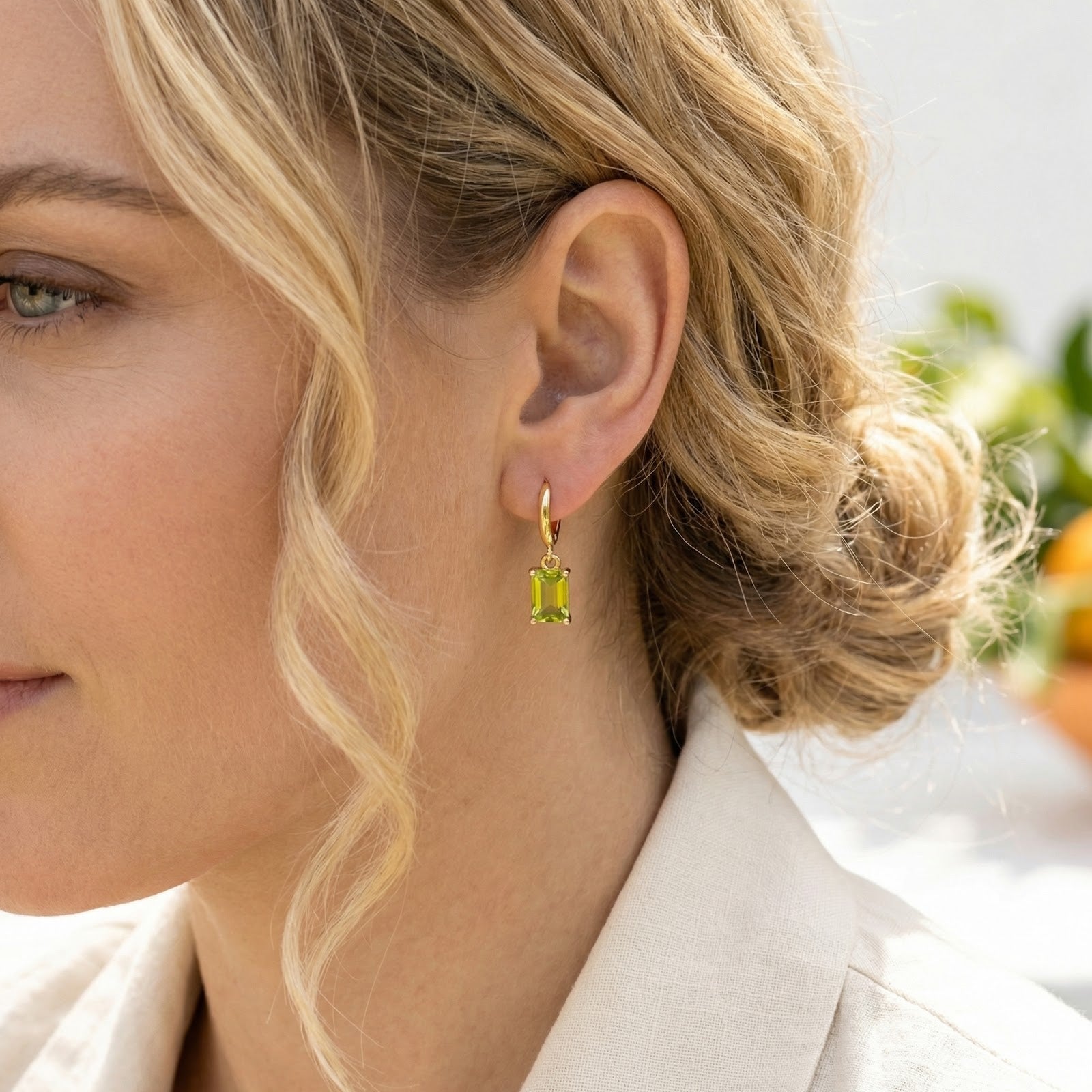 Side profile of a model wearing the gold Lunaris emerald-cut simulated peridot drop hoop earring.