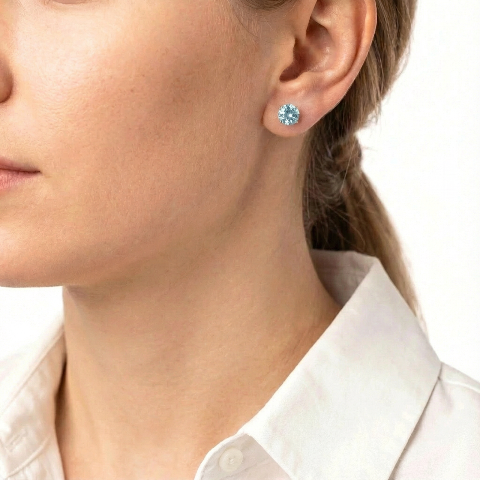 Side profile of a woman wearing a round cut simulated aquamarine sterling silver stud earring.