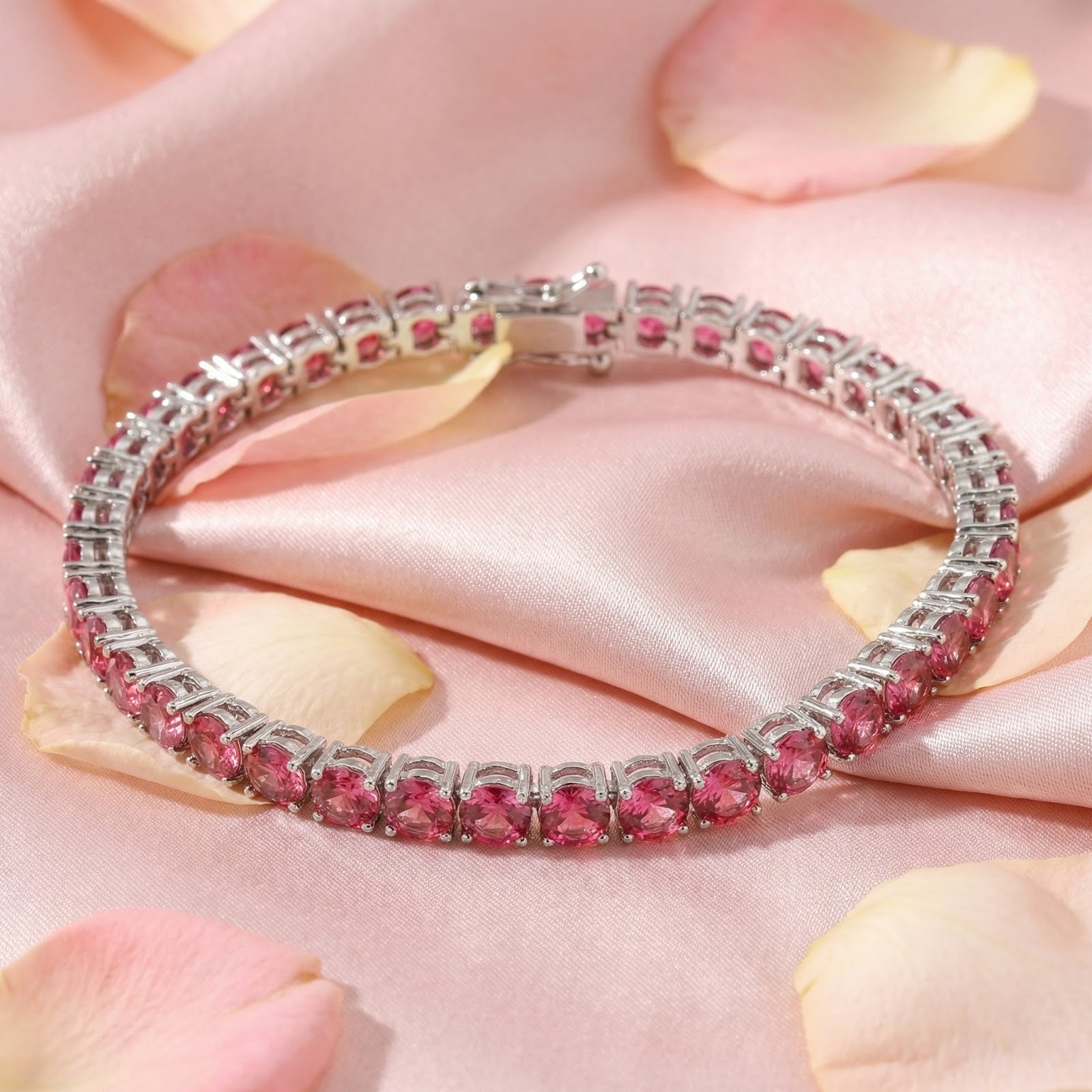 Stainless steel tennis bracelet with round-cut simulated pink tourmaline stones on pink satin and rose petals.