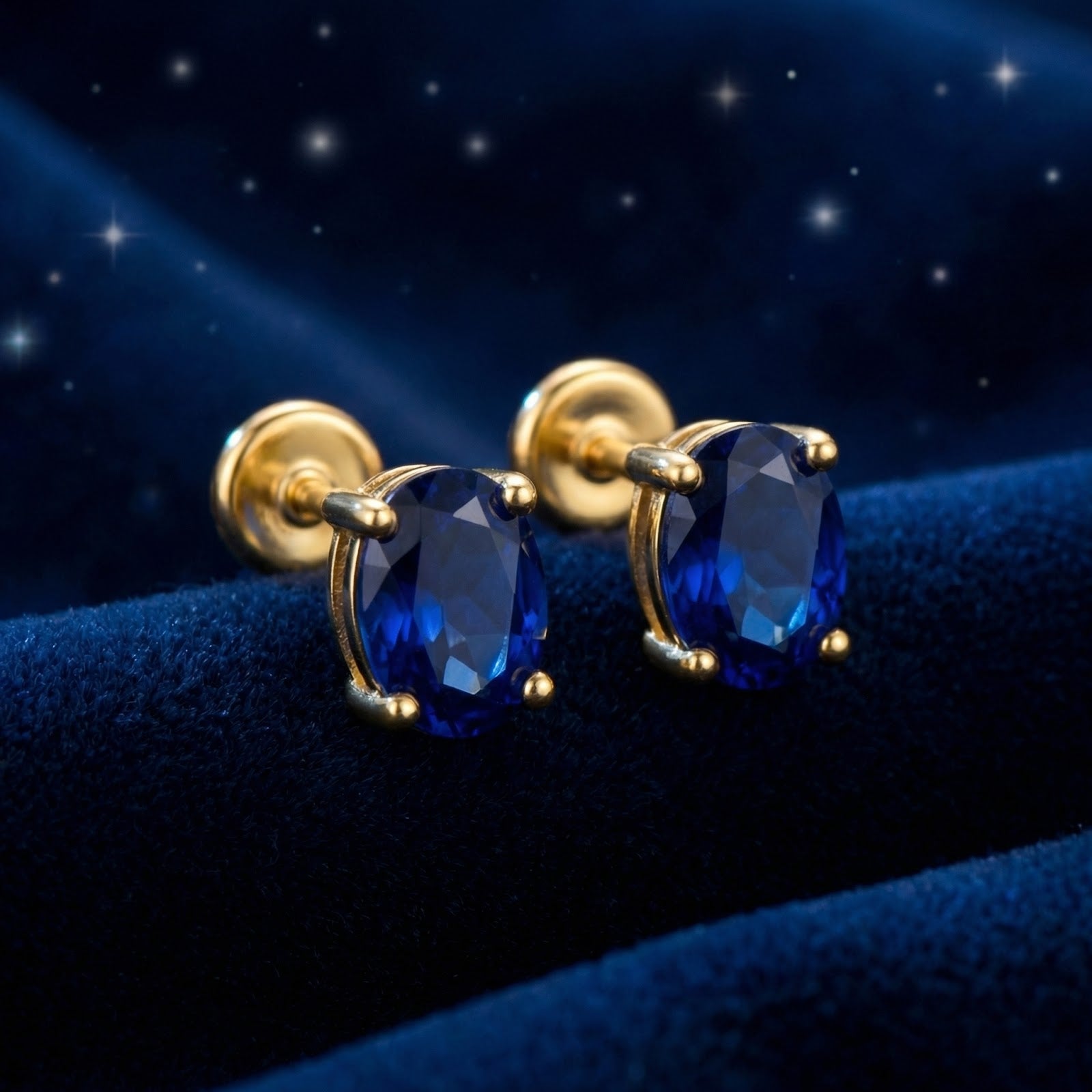 Pair of oval royal blue simulated sapphire stud earrings in 18K gold vermeil on a dark blue velvet background.