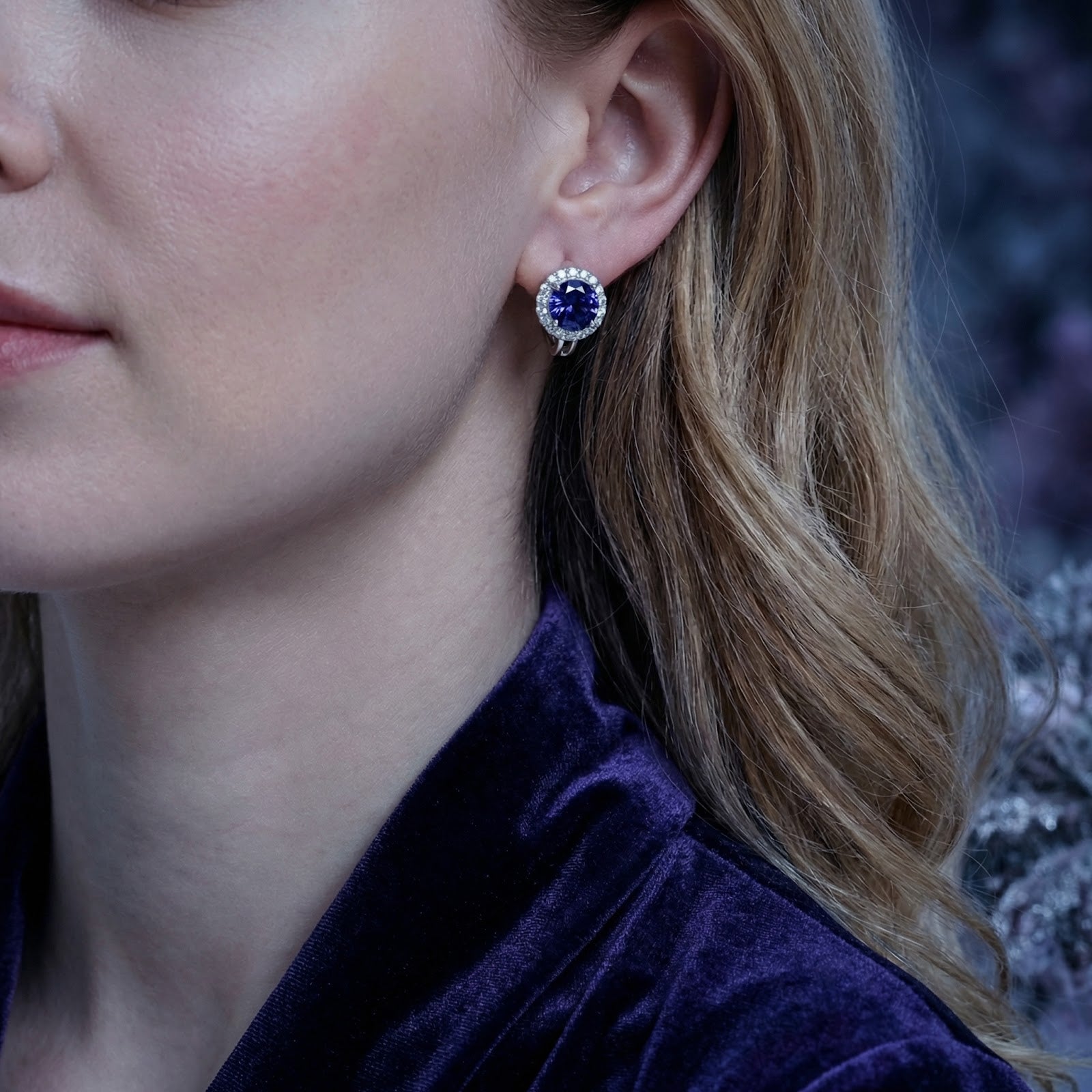 Close-up of a model wearing a round blue-violet moissanite halo stud earring in S925 sterling silver.
