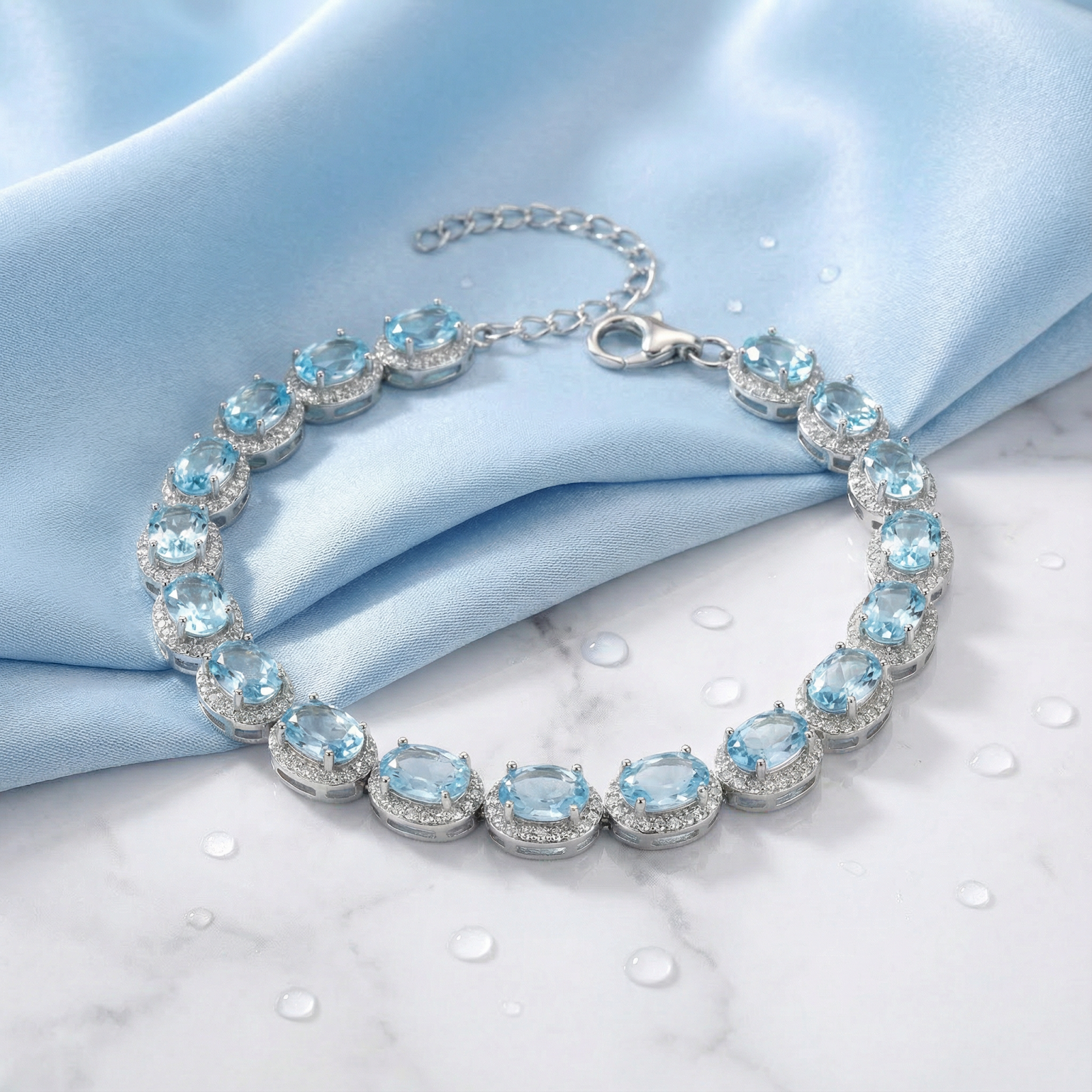 Oval cut simulated aquamarine halo bracelet in sterling silver on blue silk and marble background.