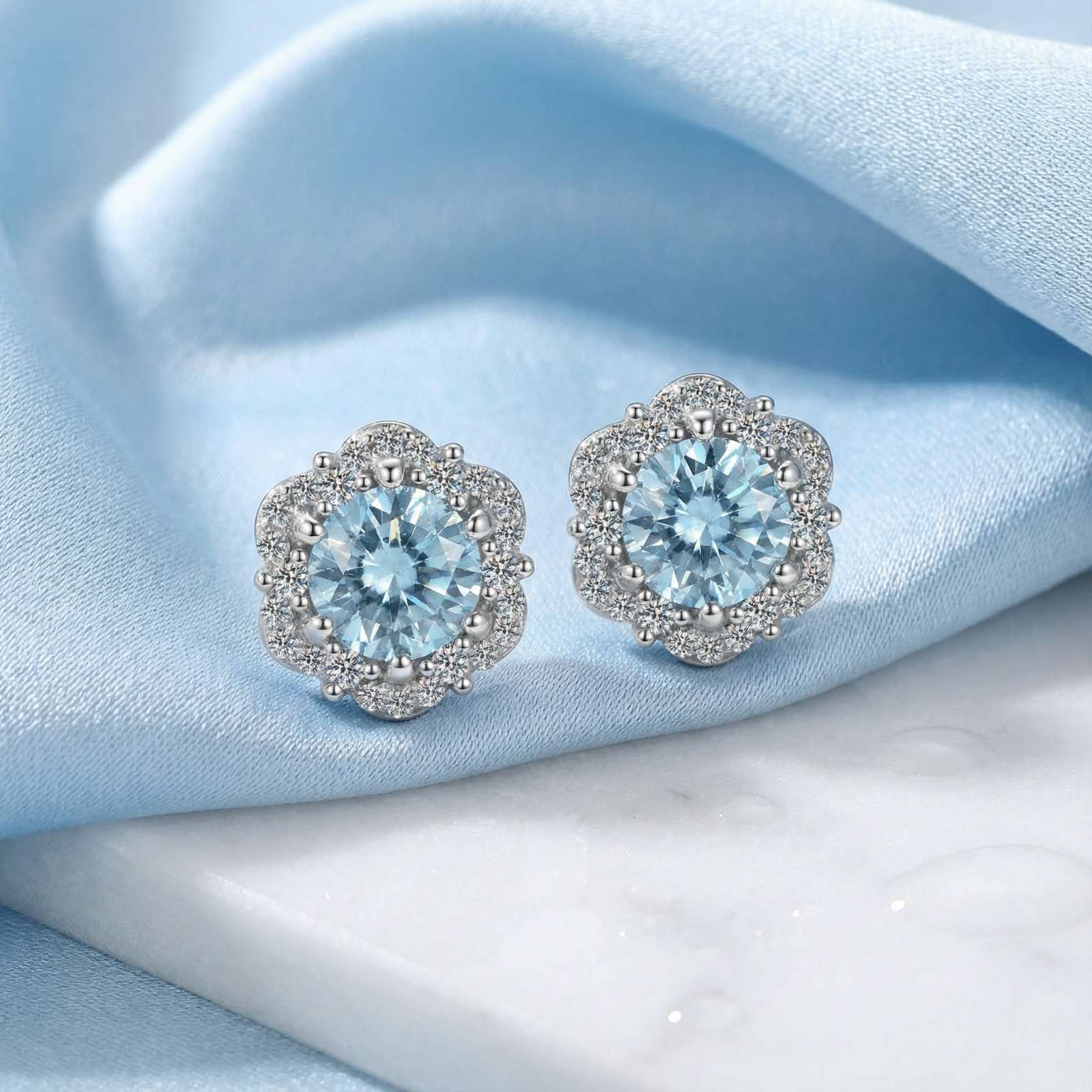 Round cut simulated aquamarine halo stud earrings in S925 sterling silver on light blue silk and marble.