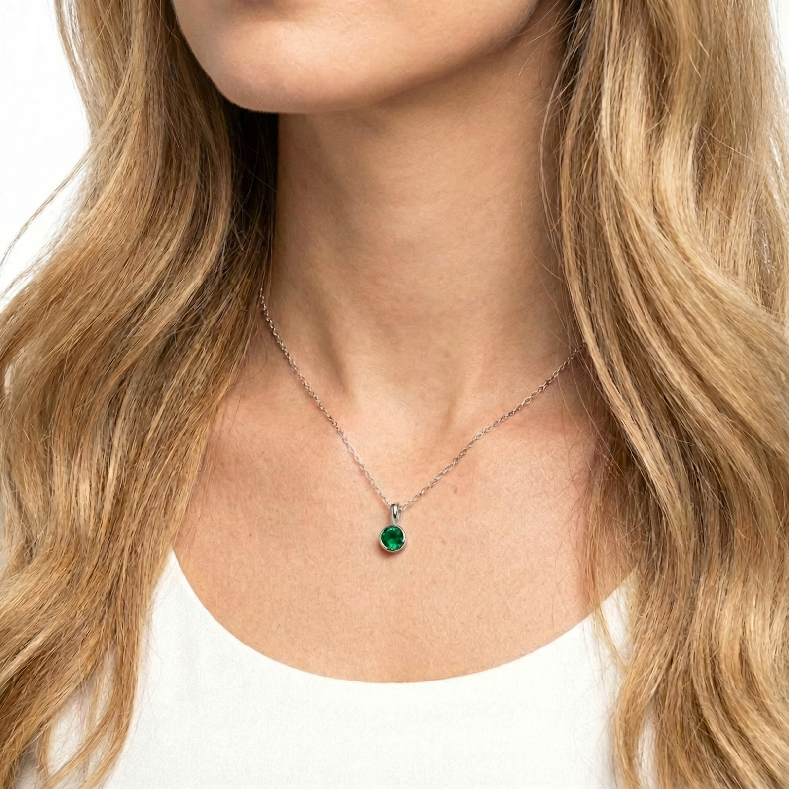 Close-up of a round green simulated emerald bezel pendant on a sterling silver chain worn by a model.