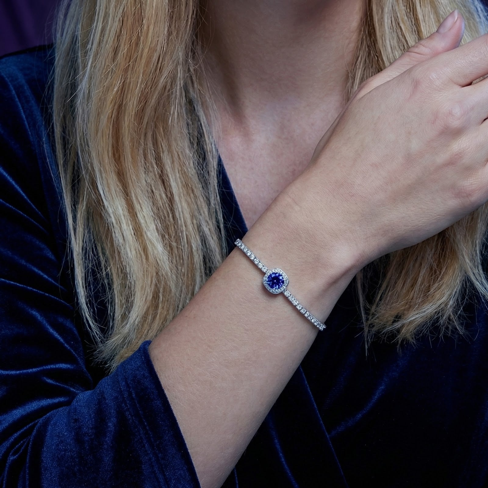 Adjustable sterling silver halo bracelet with a blue-violet simulated tanzanite worn on a woman's wrist.
