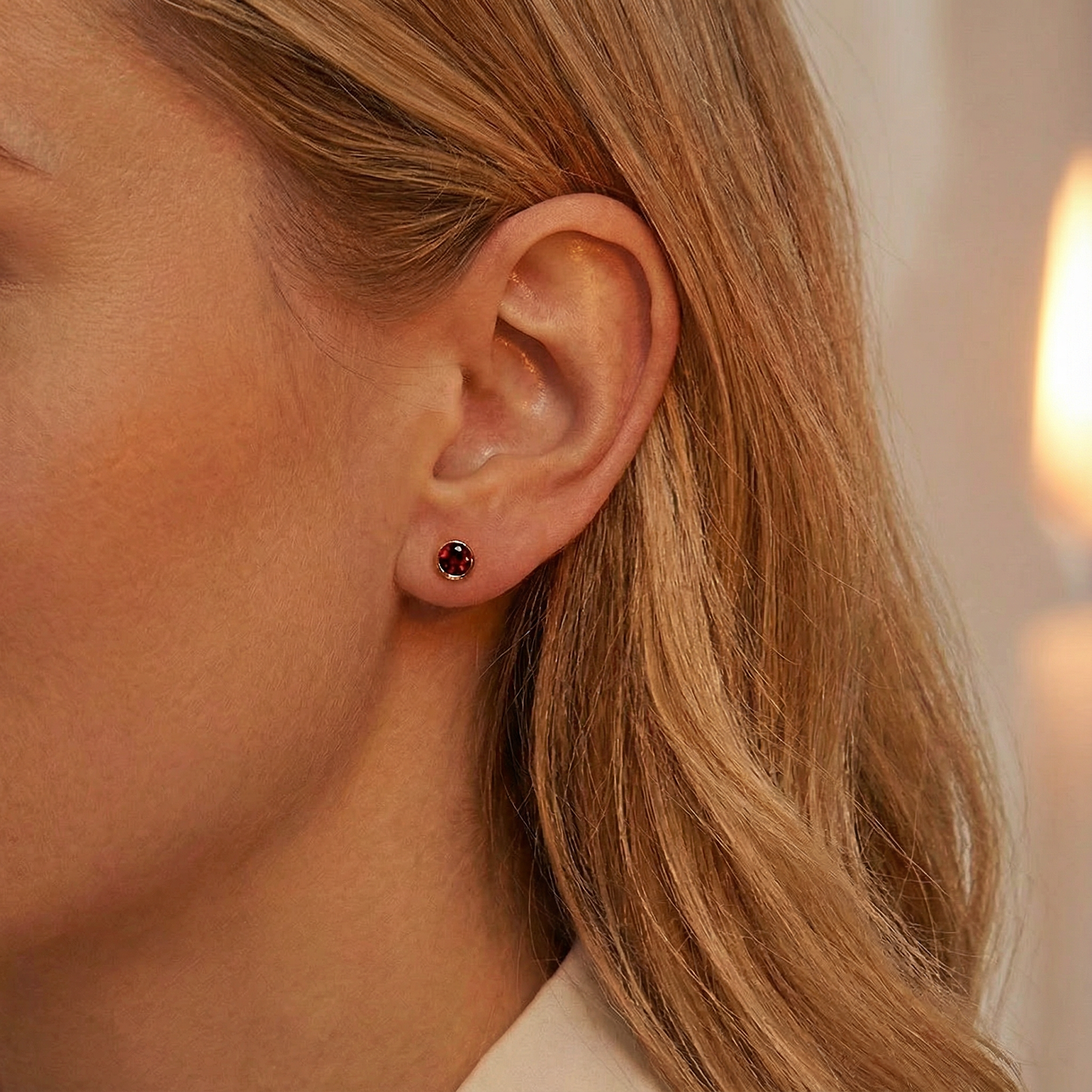 Woman wearing a round red simulated garnet stud earring in an 18K gold vermeil bezel setting.