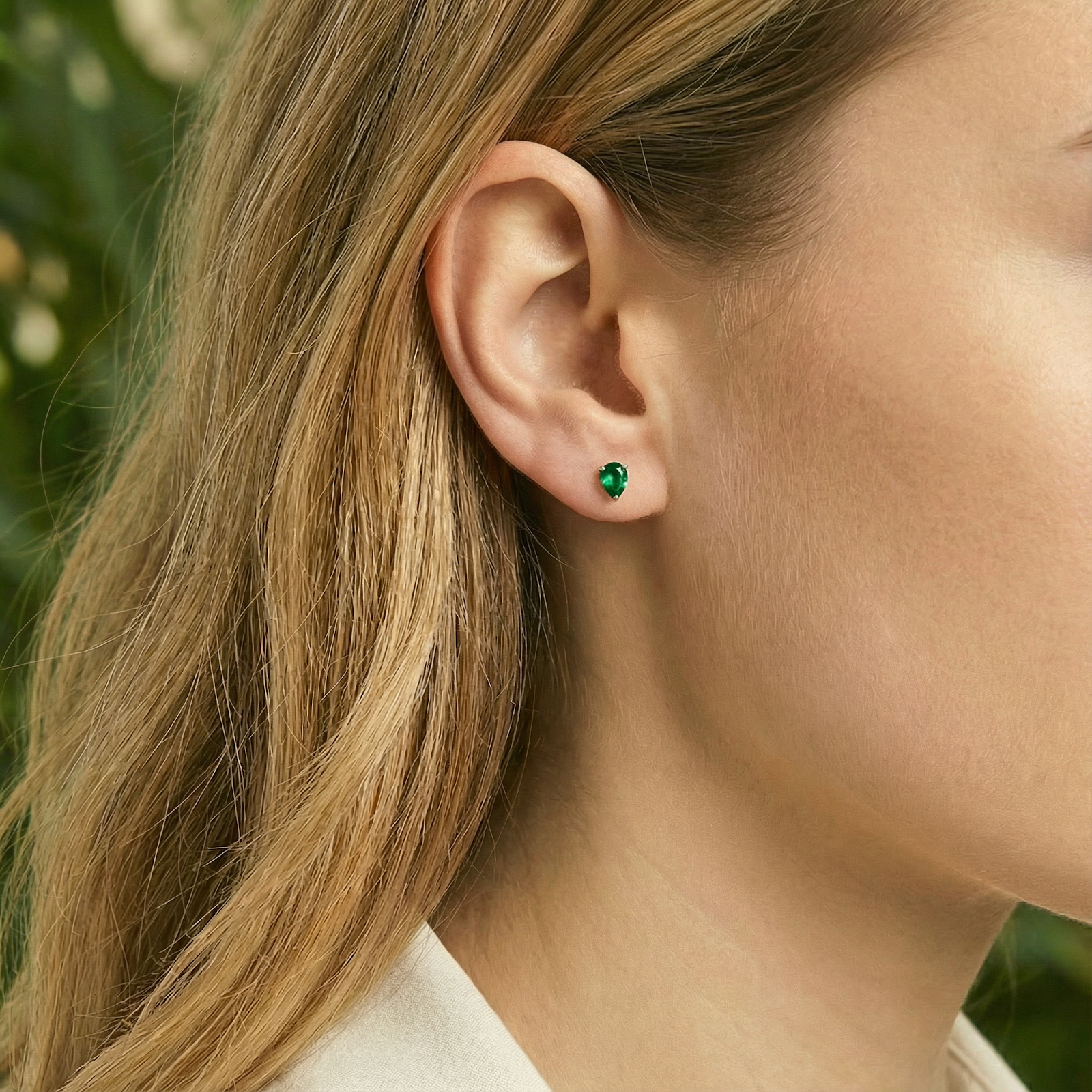 Model wearing a pear-cut simulated emerald stud earring in 18K gold vermeil on her earlobe.