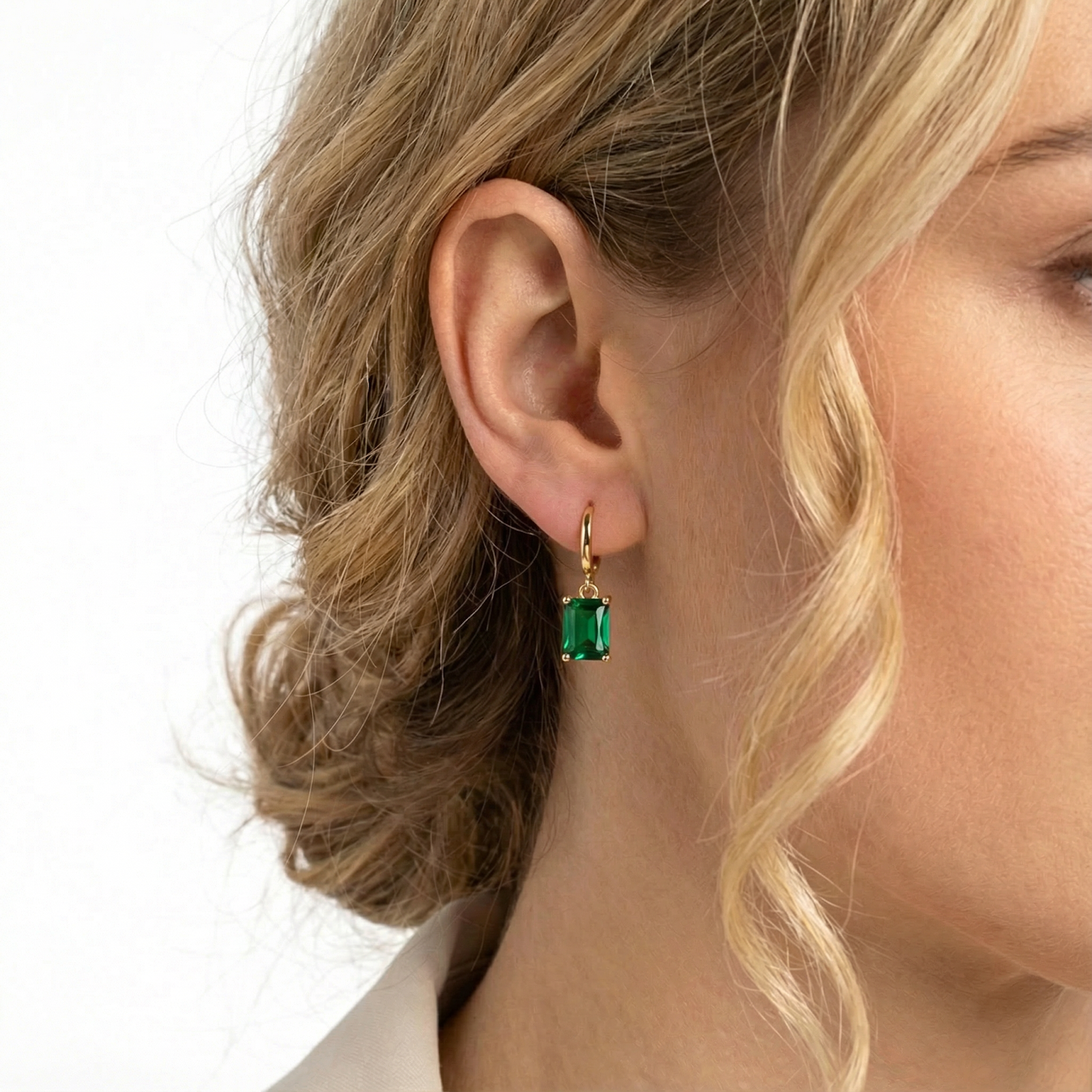 Close-up of a woman's ear wearing a gold vermeil hoop earring with a rectangular emerald-cut green stone.
