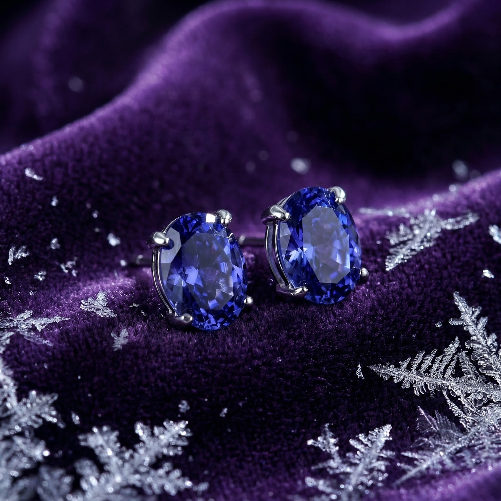 Oval cut simulated tanzanite stud earrings in sterling silver on purple velvet with winter snowflake accents.
