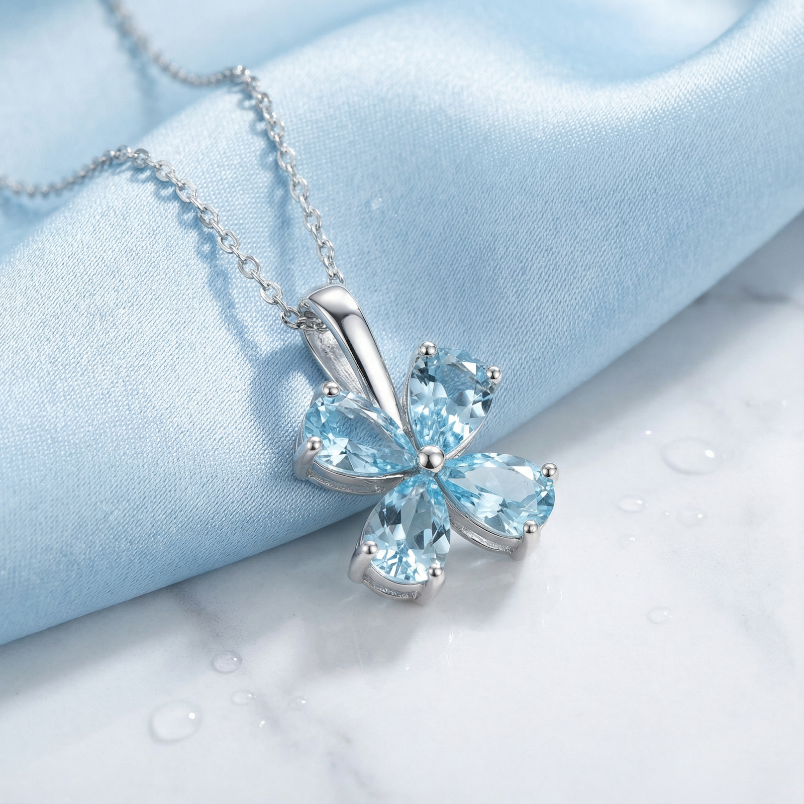 Solara clover necklace in S925 sterling silver with pear-cut simulated aquamarines on blue silk with water droplets.
