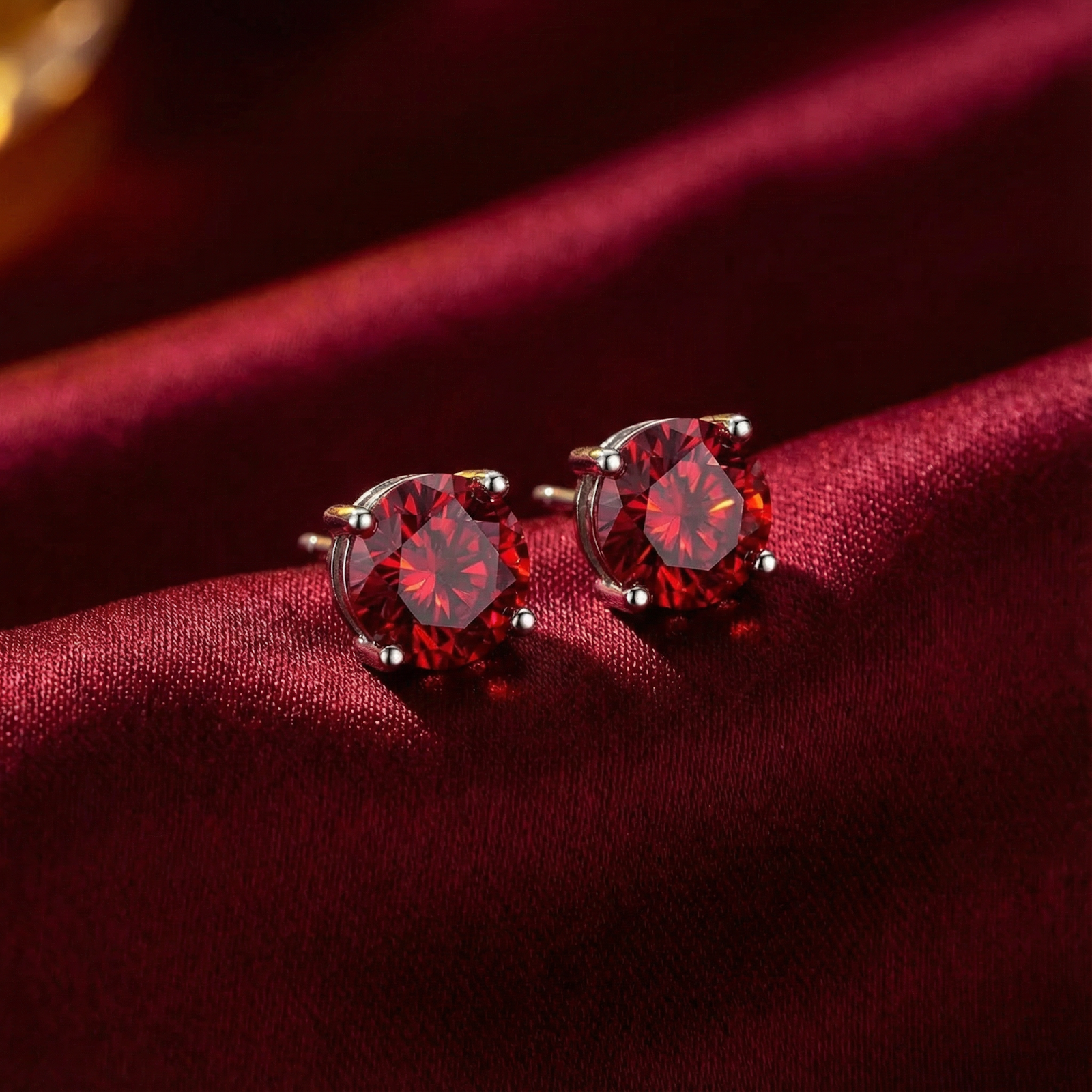 Macro view of round cut simulated ruby stud earrings with sterling silver four-prong settings on red satin.