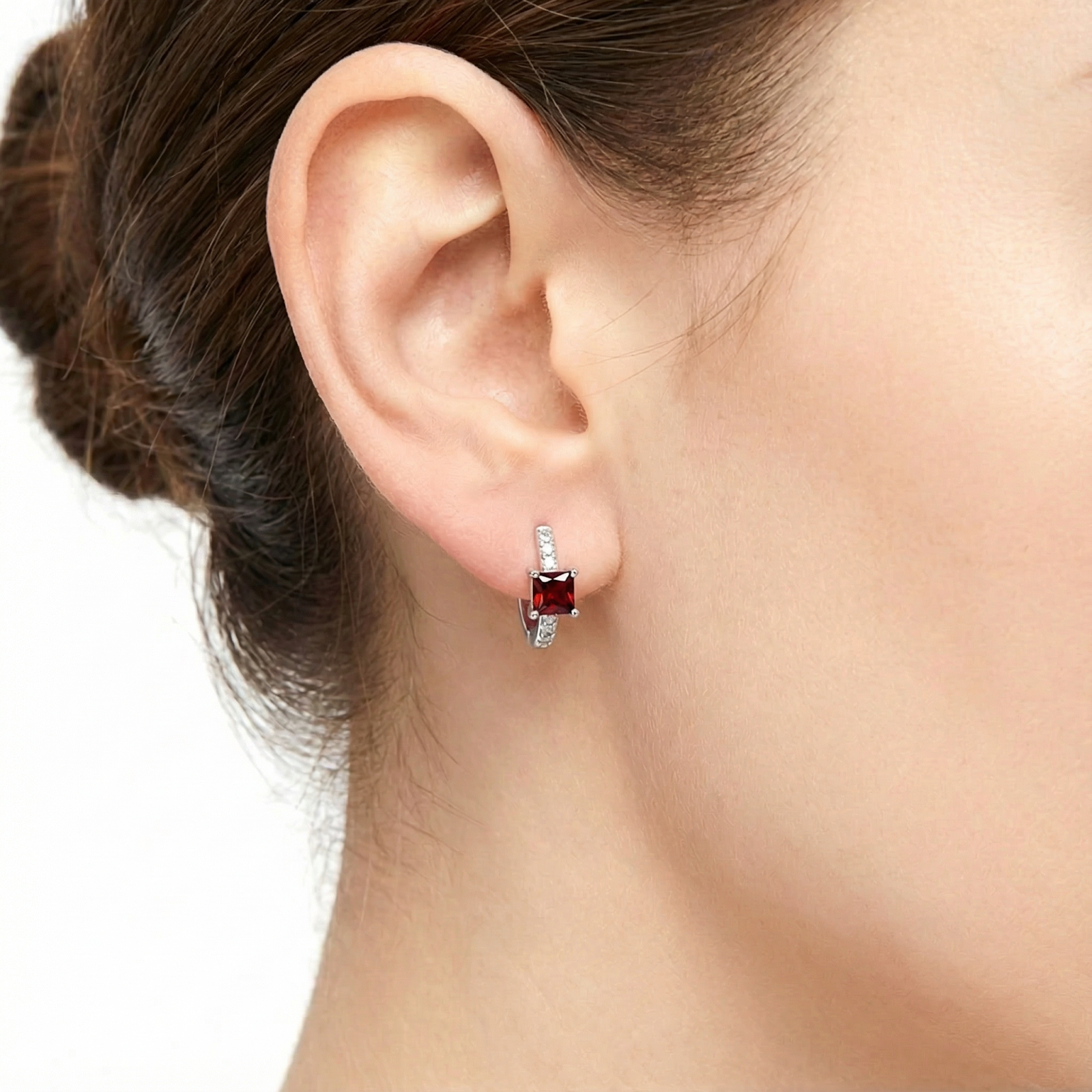 Close-up view of a princess cut red garnet huggie earring worn on a model's ear.