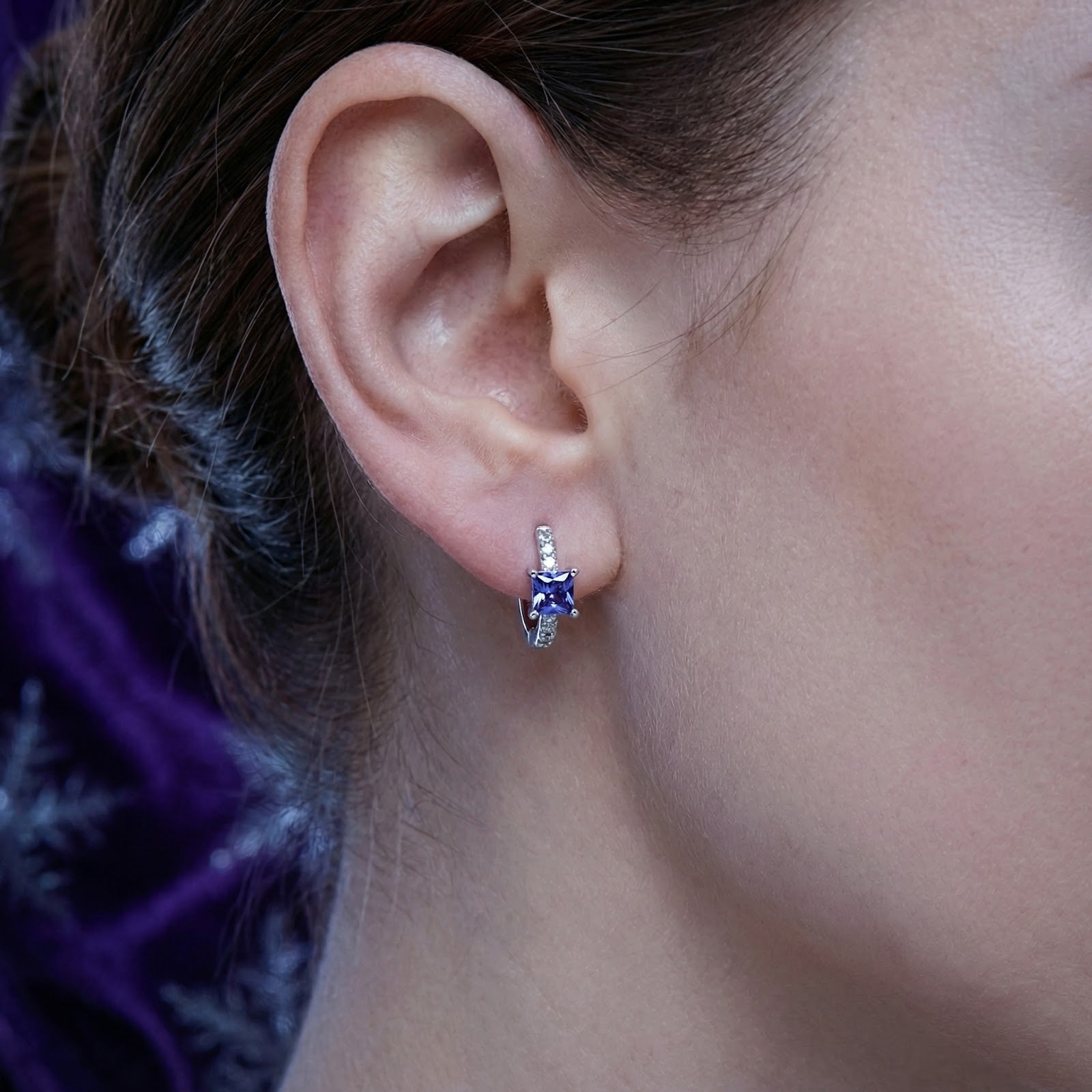 Close-up of a sterling silver hoop earring with a square-cut simulated tanzanite worn on an ear.