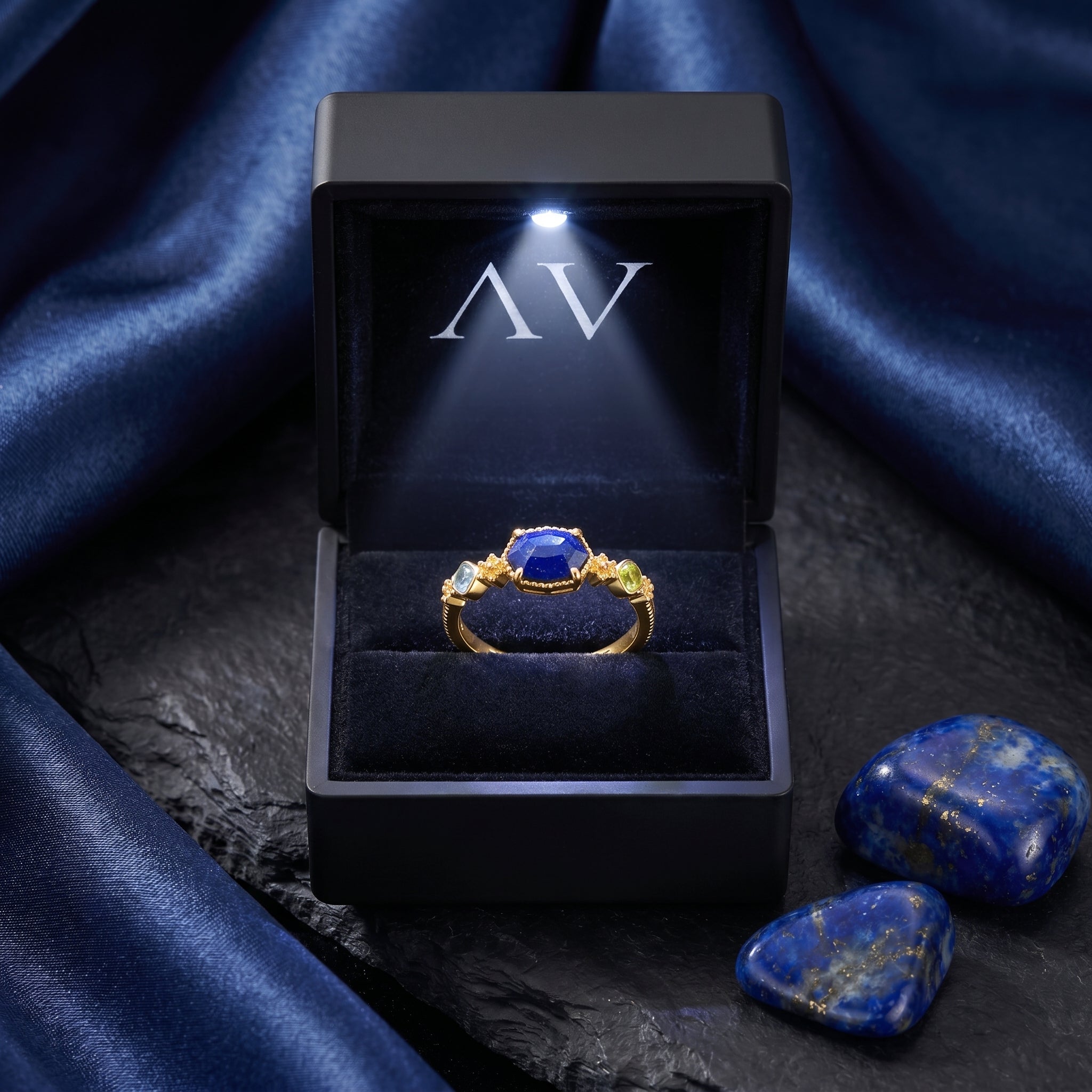 Gold lapis lazuli ring presented in a black LED-lighted jewelry box on a dark stone surface.