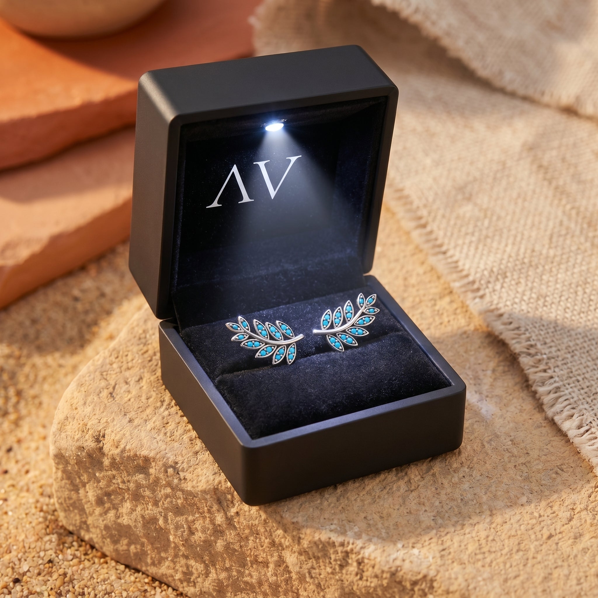 Silver Taos Turquoise leaf earrings with round stones in a black LED-lighted gift box on a sandy stone surface.
