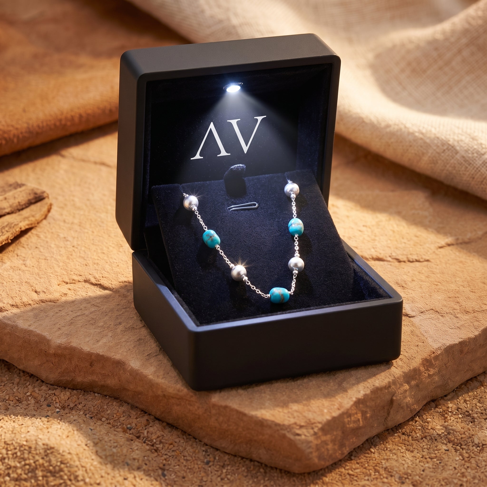 Turquoise and silver necklace in a black LED-lit jewelry box on a stone background.