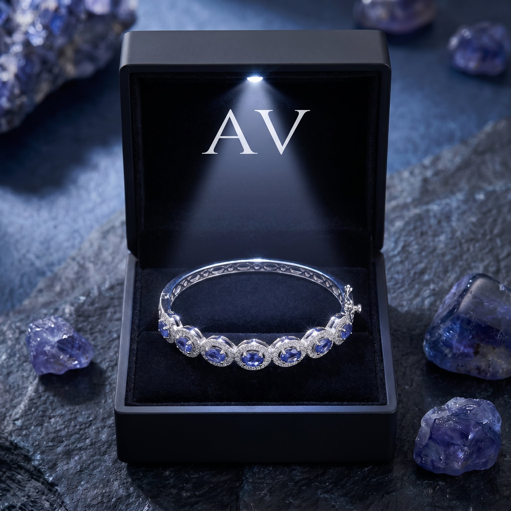 Sterling silver tanzanite bracelet presented in a black lighted gift box on a dark stone surface.
