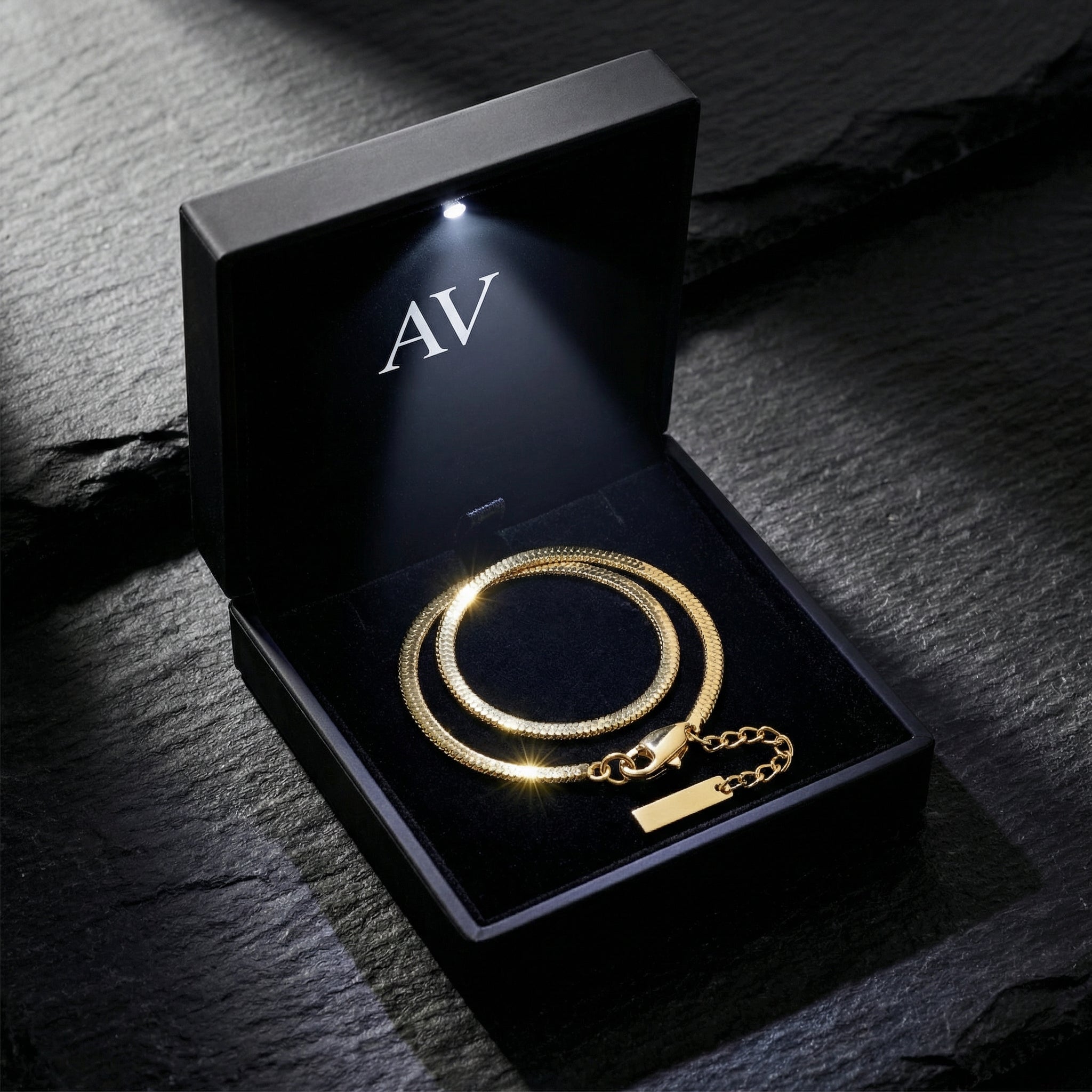 Gold-tone stainless steel square link bracelet inside a premium black LED-lit gift box with AV logo.