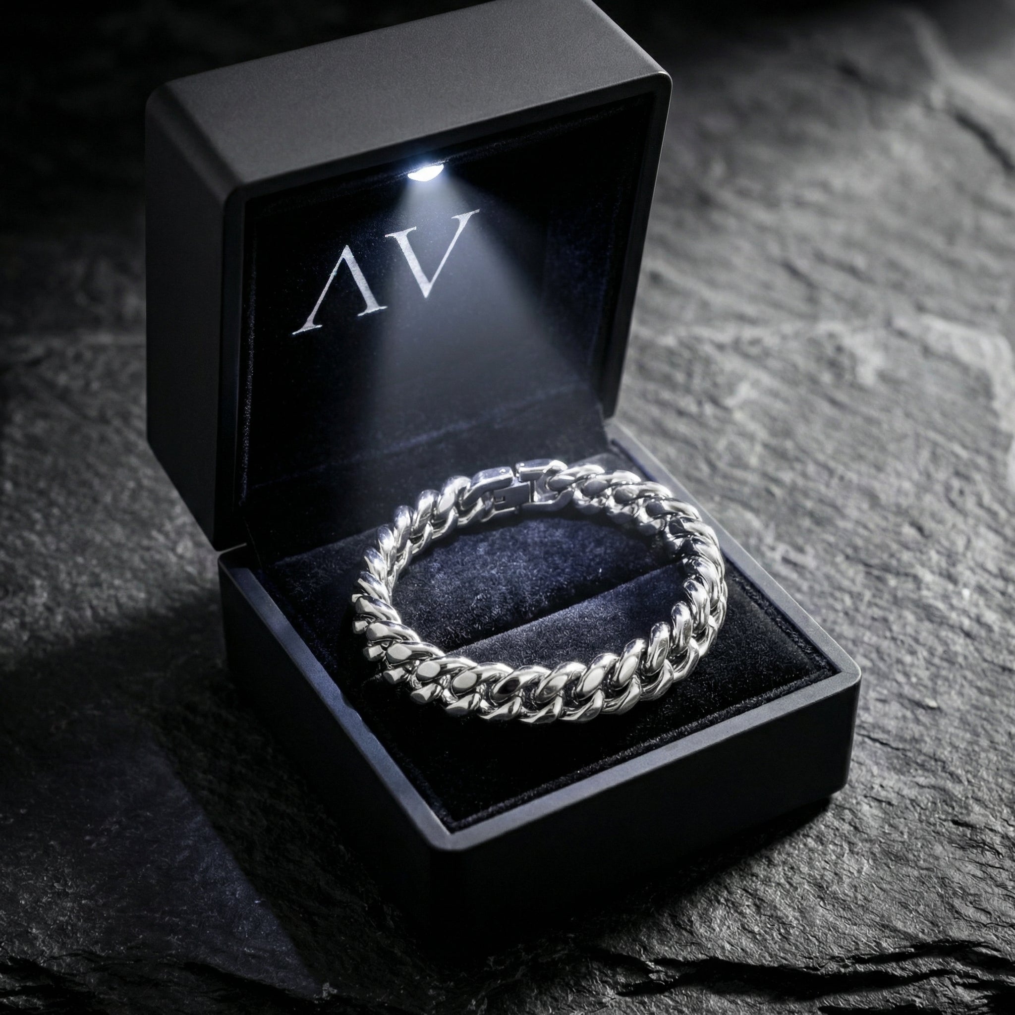Men's silver stainless steel Cuban link bracelet inside a black LED-lit gift box on a stone surface.
