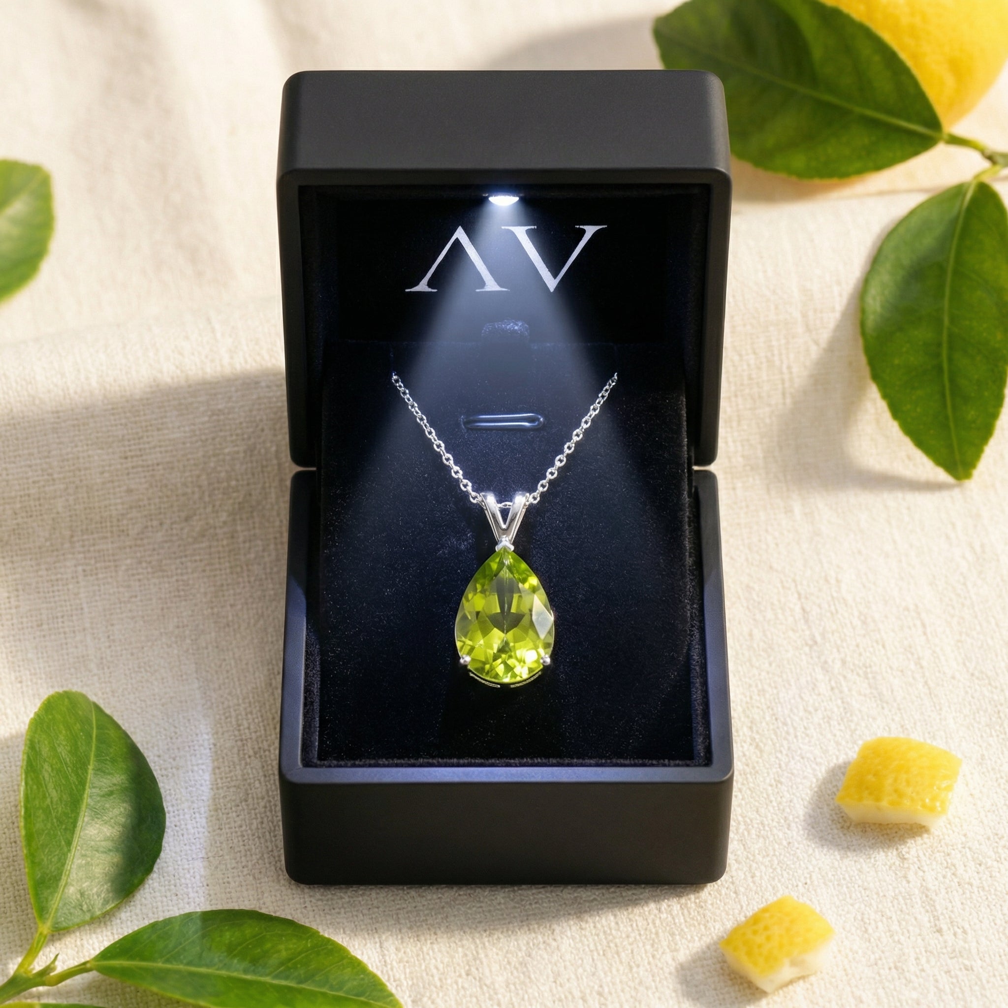 Pear-cut green moissanite necklace in sterling silver inside a lighted black jewelry presentation box.