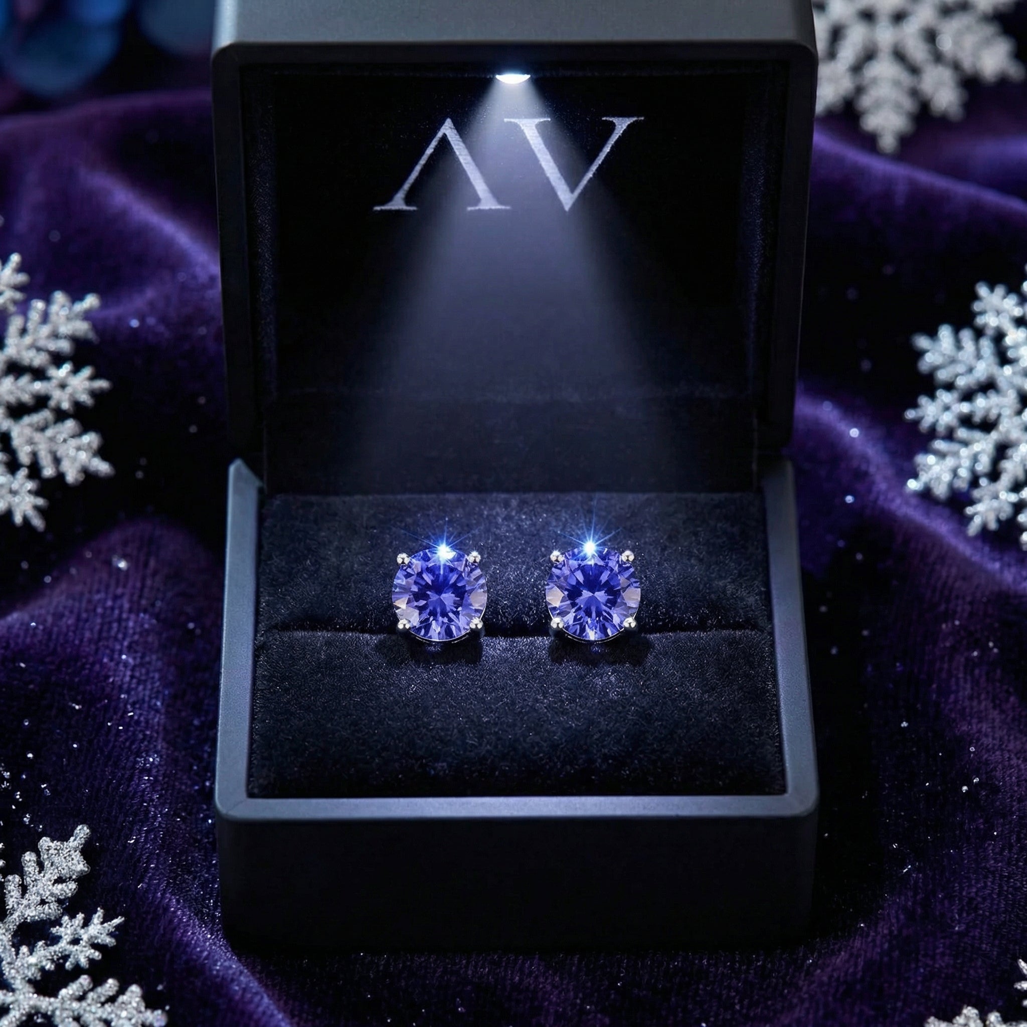 Round cut simulated tanzanite silver studs in a lighted black presentation box on purple velvet.