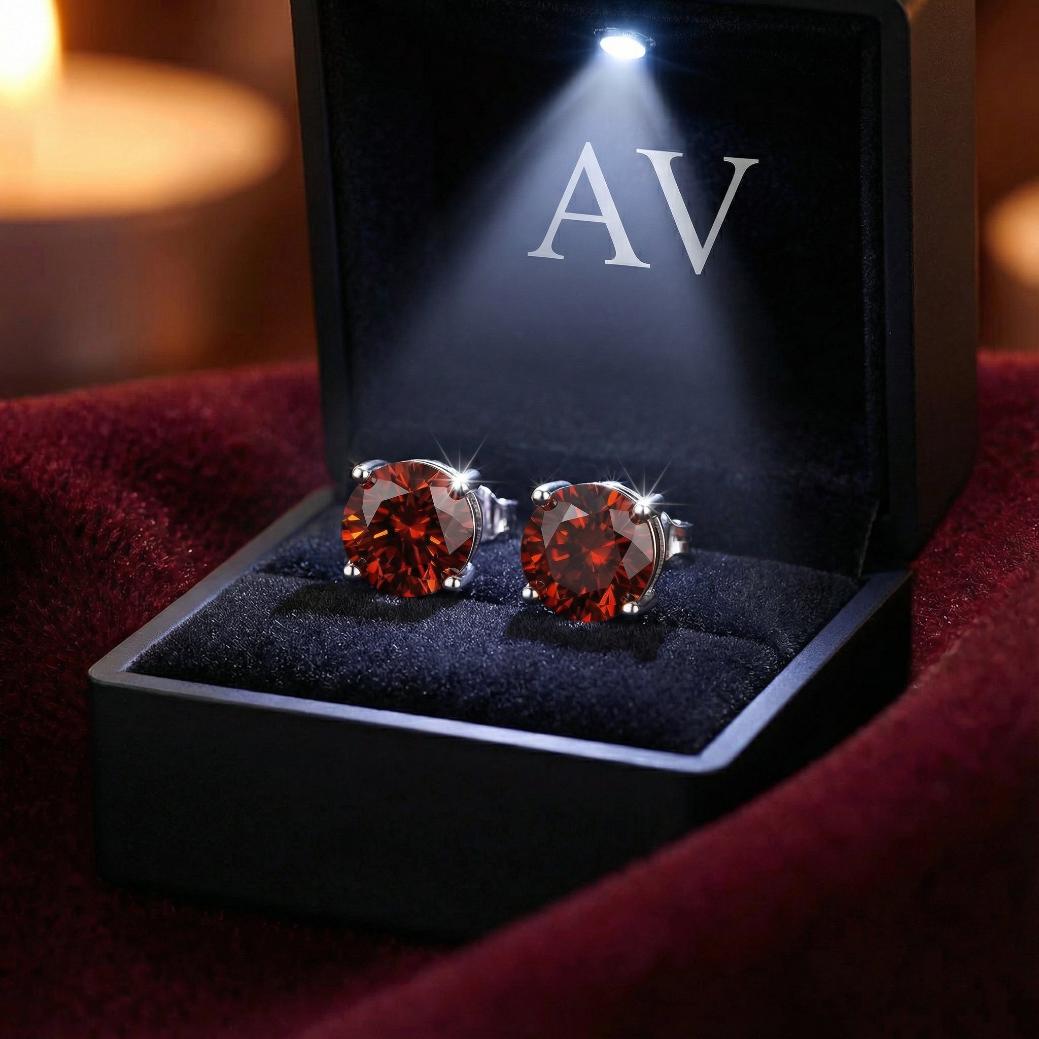 Pair of round cut simulated garnet stud earrings in a lighted black jewelry box with AV branding.