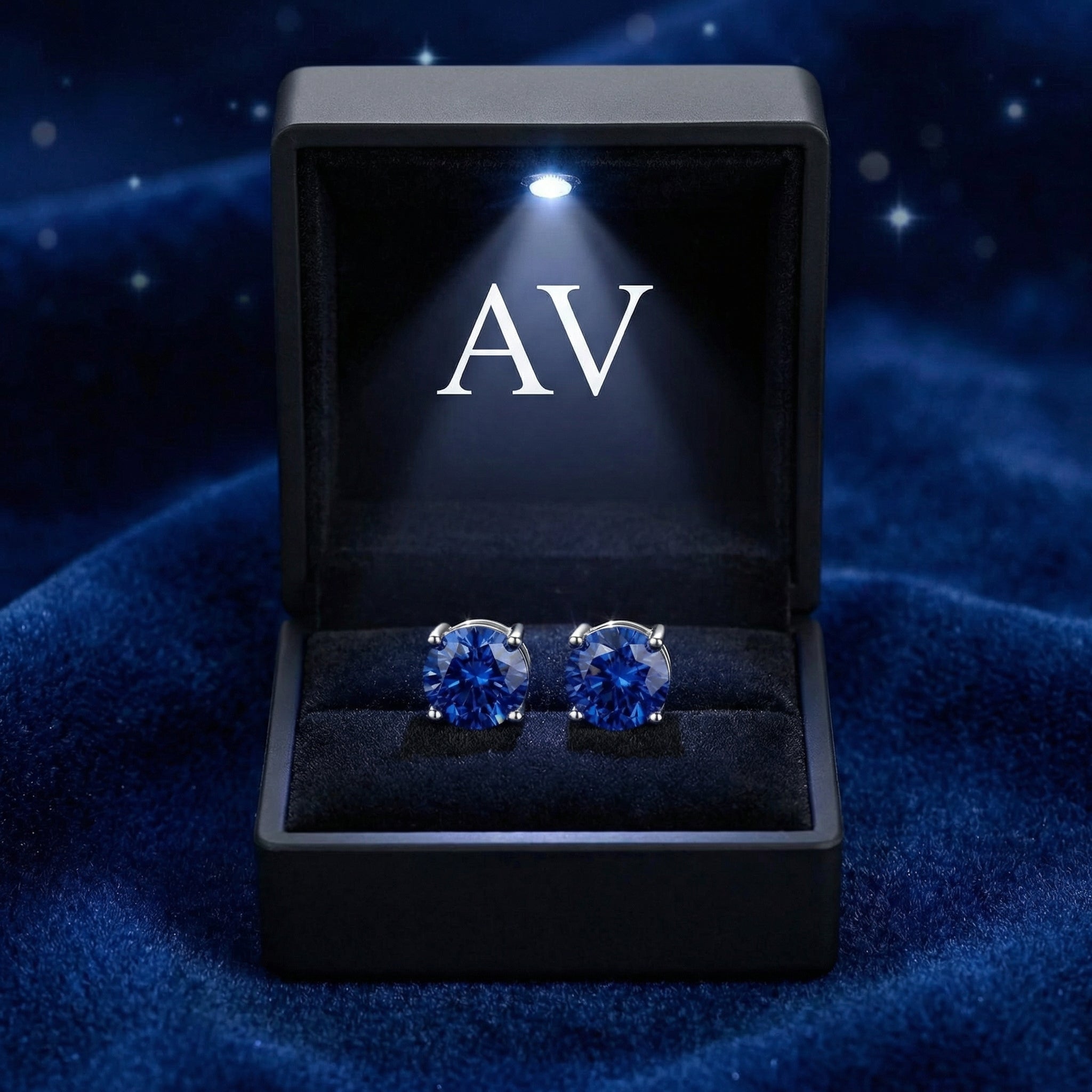 Round blue simulated sapphire stud earrings presented in a lighted black jewelry box with a silver AV logo.