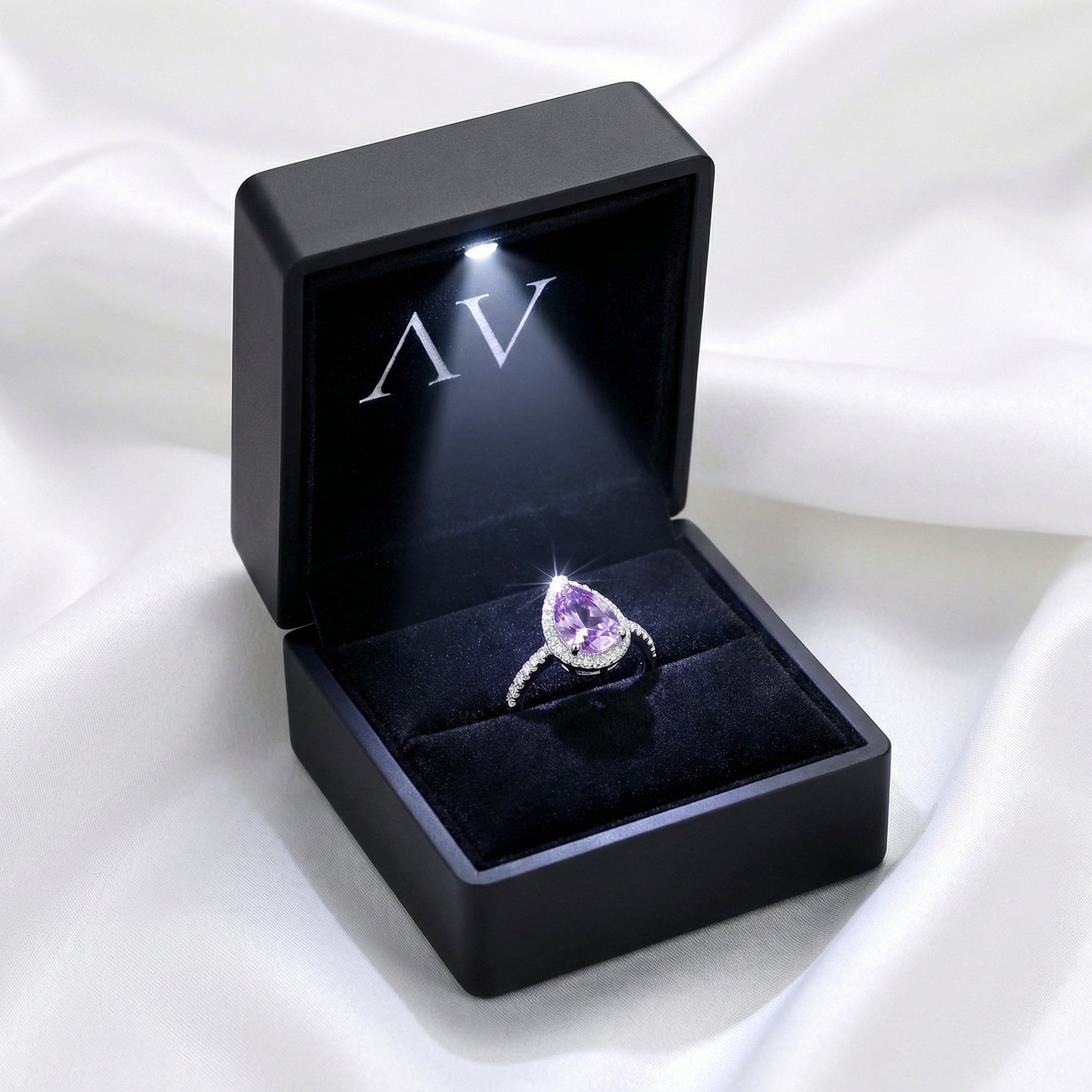 Teardrop simulated amethyst ring in a black LED-lit jewelry box on a white fabric background.