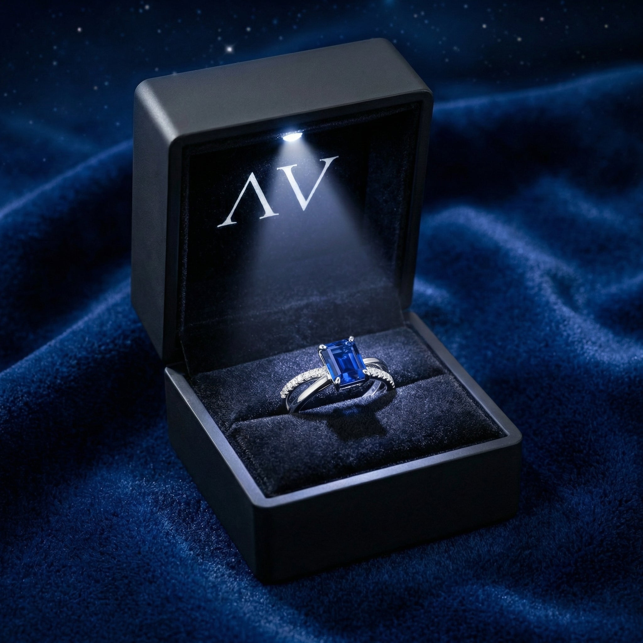 Emerald-cut simulated sapphire crossover ring presented in a black LED-lit jewelry gift box on blue velvet.
