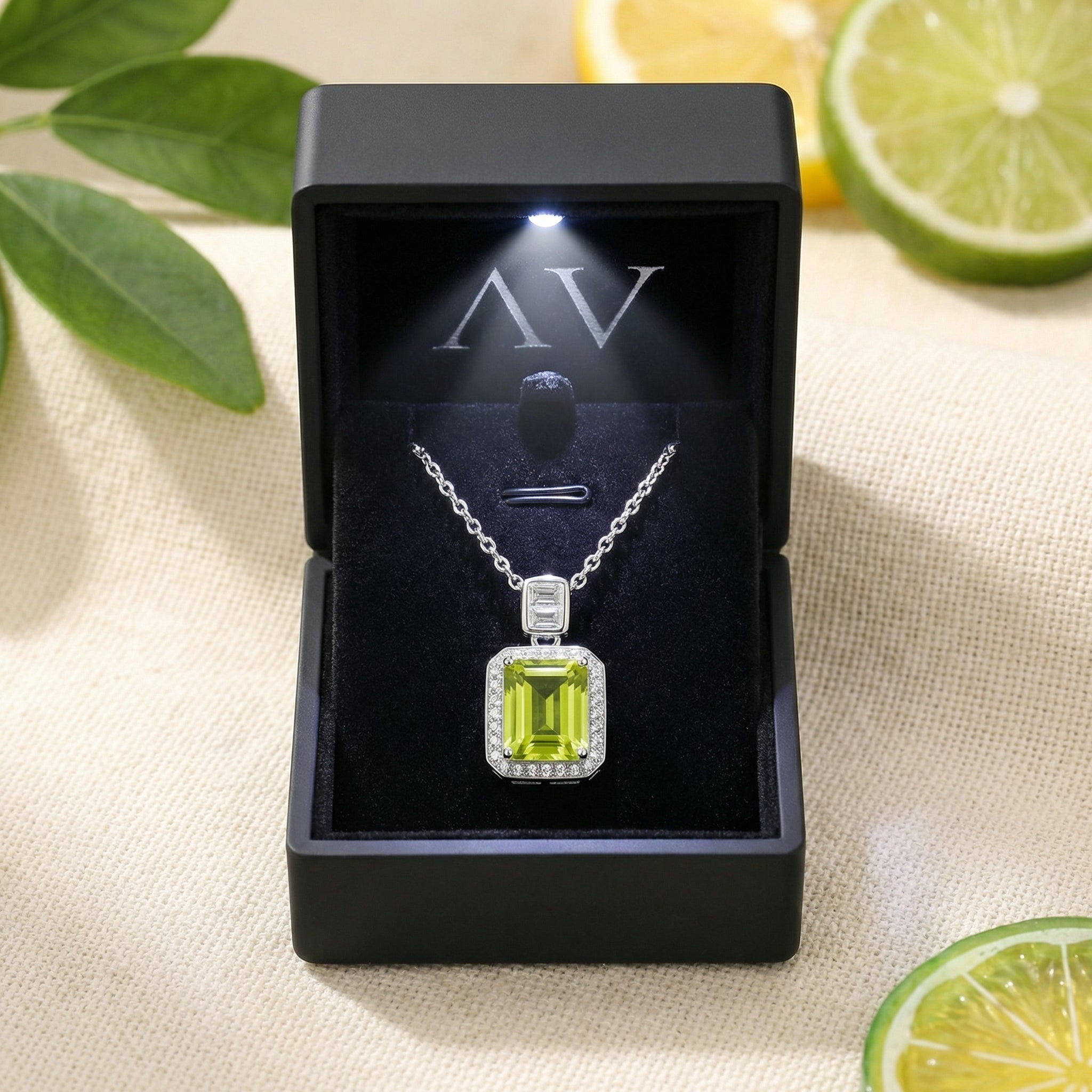 The Elianara peridot necklace displayed in a premium lighted black jewelry box with citrus fruit accents.