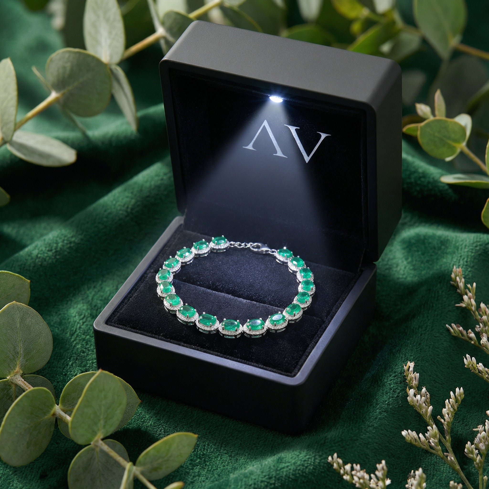 Sterling silver simulated emerald halo bracelet inside a black lighted jewelry presentation box on green velvet.