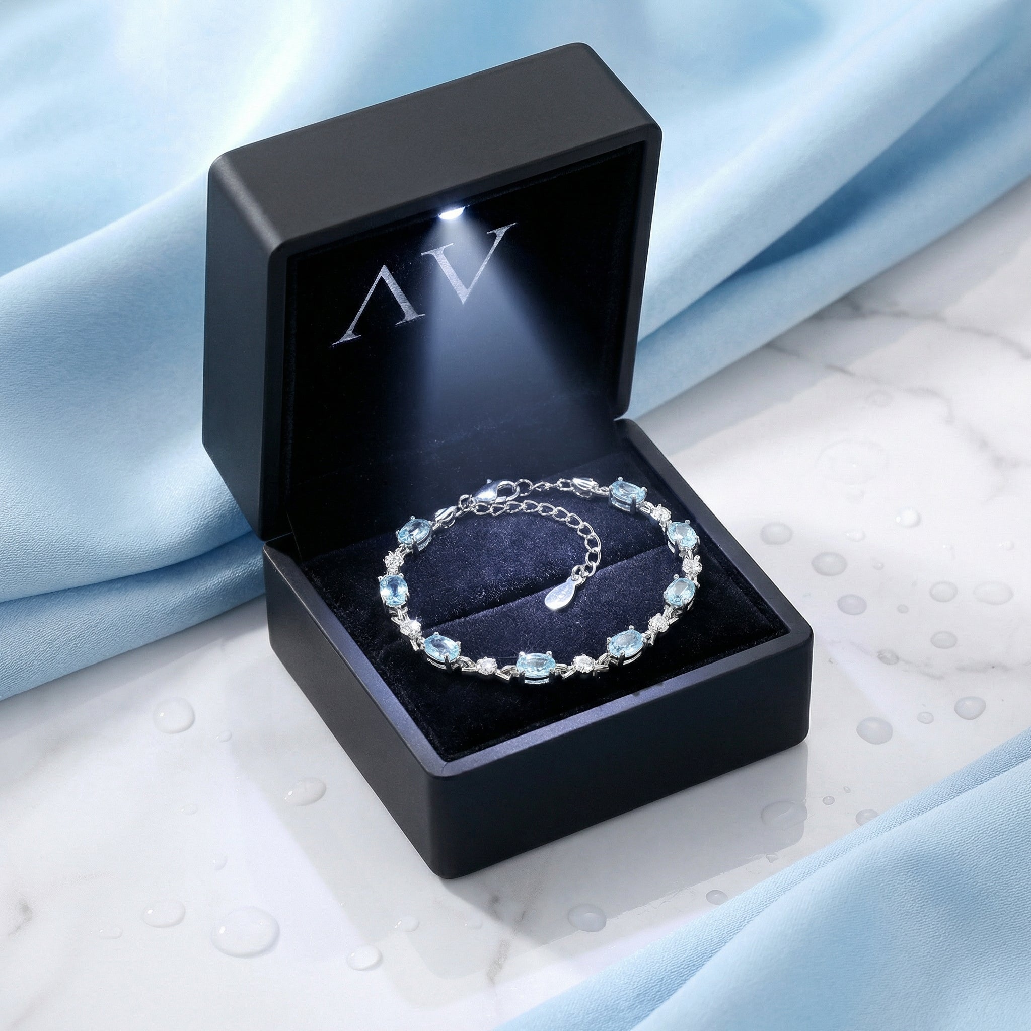 Melodia sterling silver aquamarine bracelet presented in a black lighted gift box on a blue fabric background.