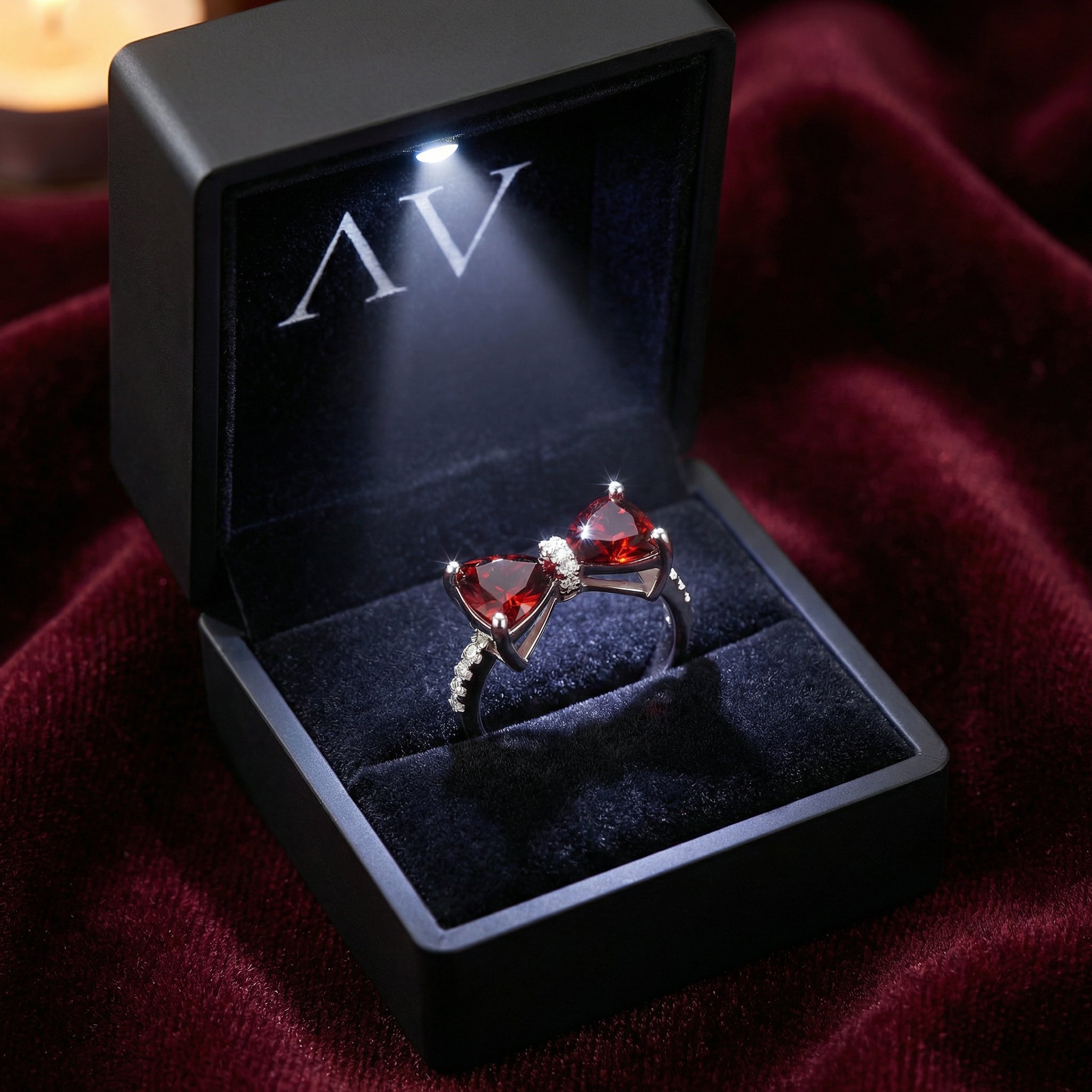 Sterling silver red garnet bow ring presented in a black LED-lit jewelry box on red velvet.