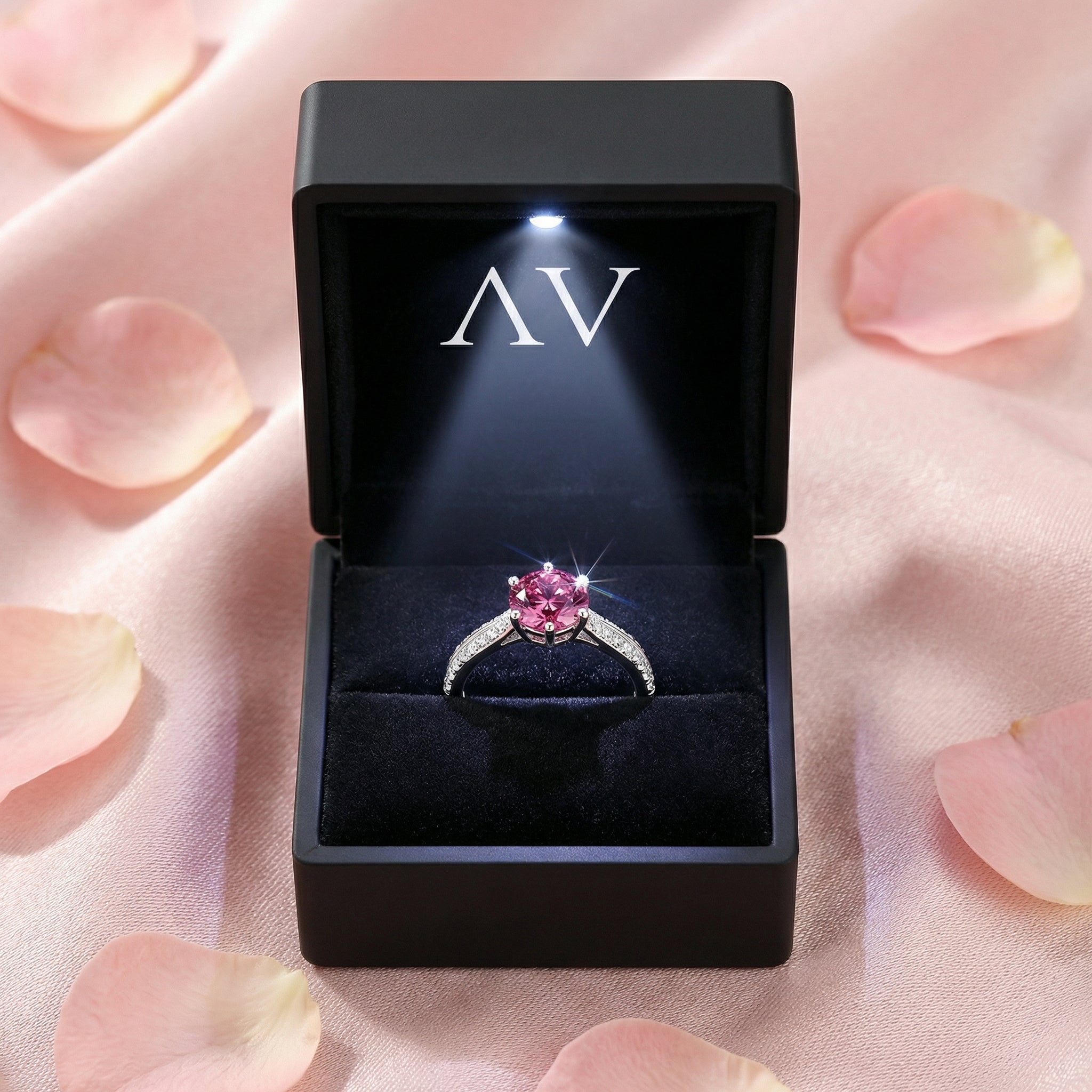 Rhosielle pink tourmaline ring displayed in a black LED-lit jewelry box with the AV logo and rose petals.